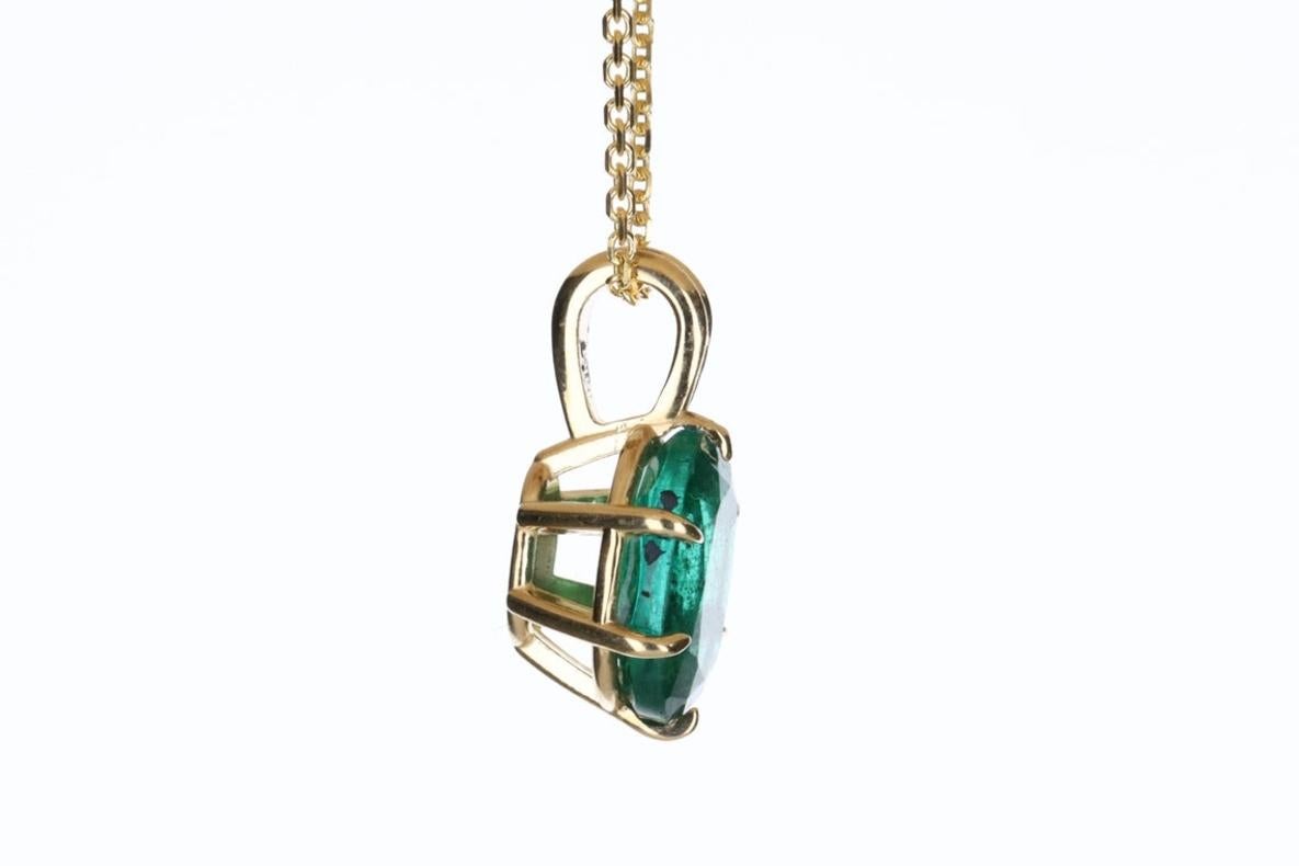 Displayed is a classic and unique emerald solitaire necklace set in 14K yellow gold. This gorgeous solitaire pendant carries a full 1.88-carat emerald in a six-claw prong setting. Fully faceted, this gemstone showcases very good shine, rare dark