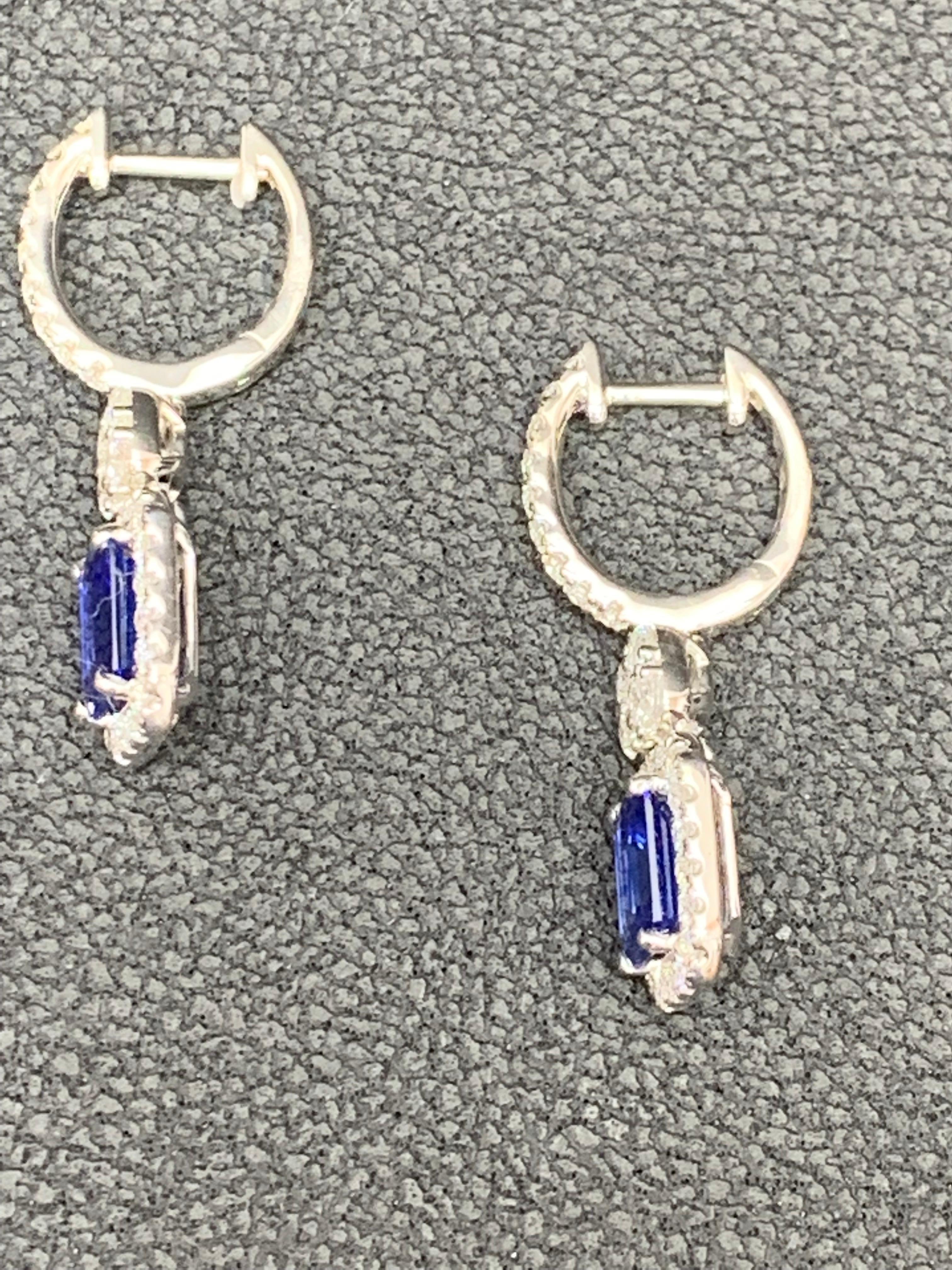 Classic 18k white gold dangle earrings set with 2 emerald cut blue sapphires weighing 1.88 carats total. The emeralds are surrounded by 1 rows of brilliant round diamonds weighing 0.62 carats suspended on an accented lever-back. A must-have piece of