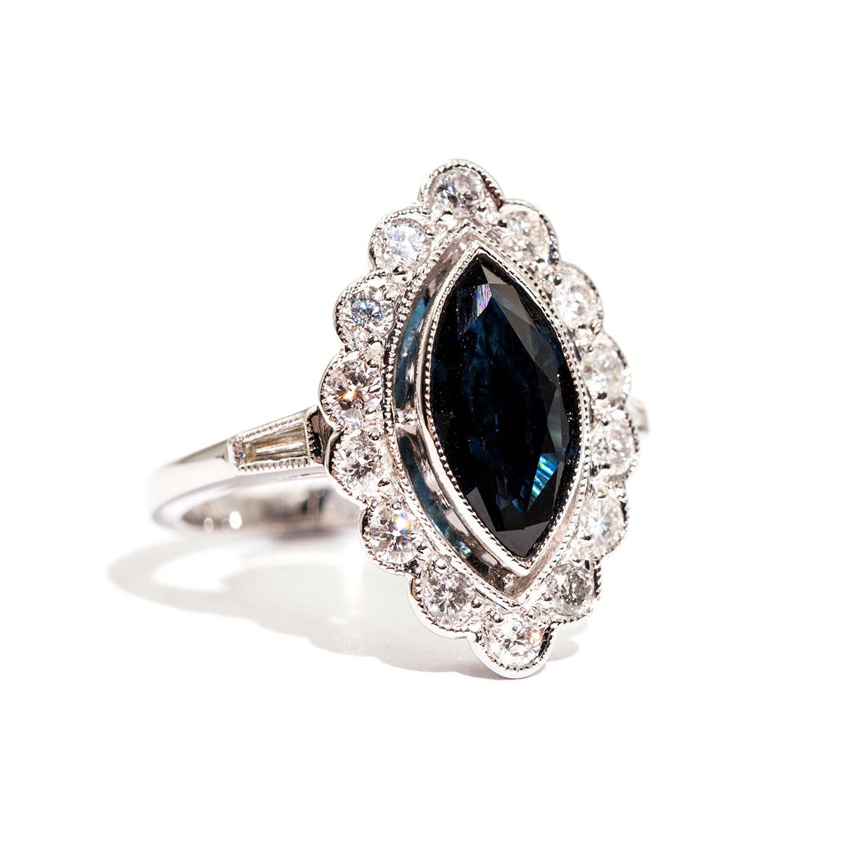 Forged in 18 carat white gold is this art deco inspired ring that features a gorgeous 1.88 carat marquise natural sapphire of a deep blue colour complimented with an alluring border of sparkling white round brilliant cut diamonds totalling 0.76