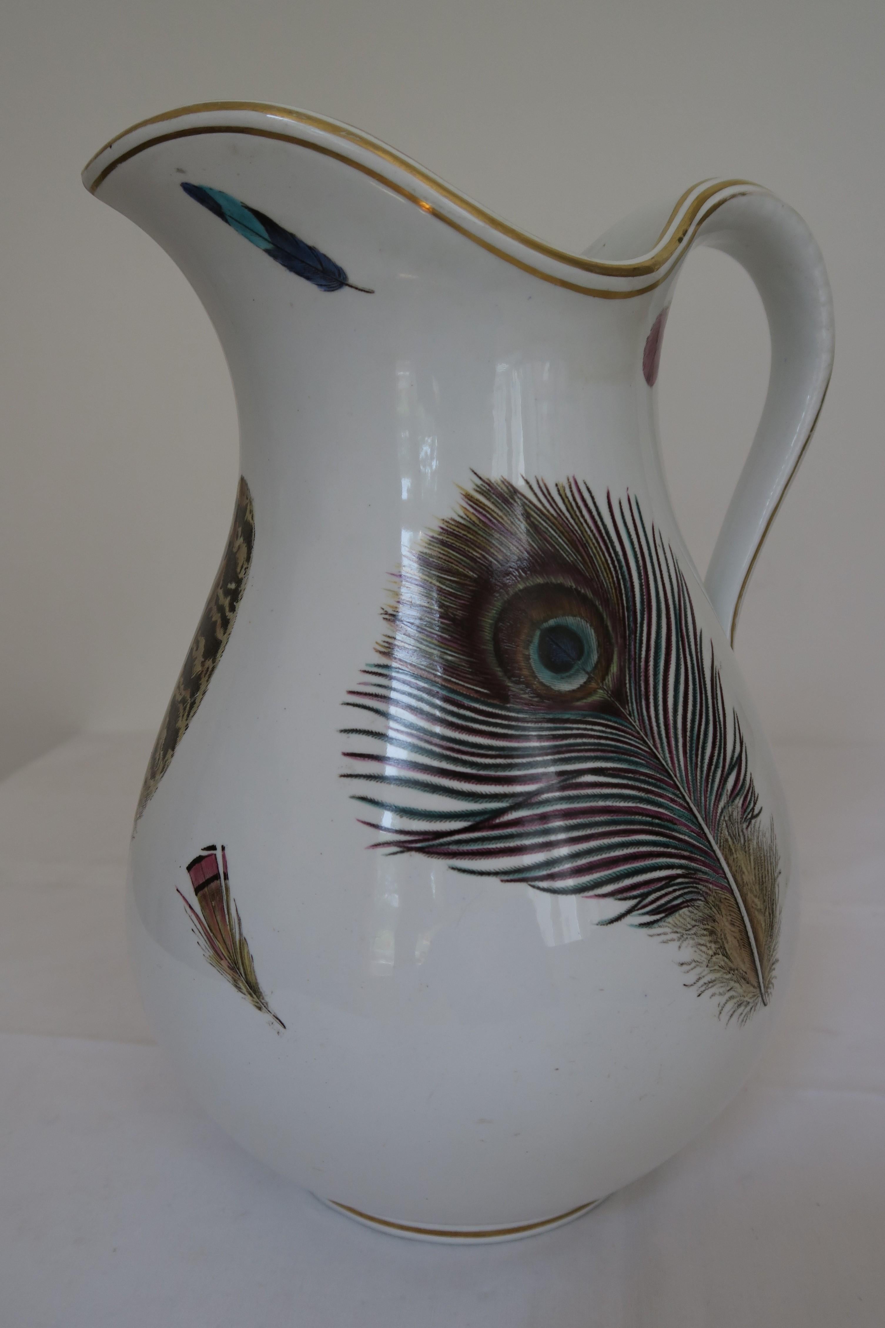 For sale is a beautiful bulbous water pitcher. It was made from porcelain by the English manufacturer Minton ca. 1880. The whole jug is covered in feather motives painted in vibrant colours Its lip and foot are decorated with a gold ring. This
