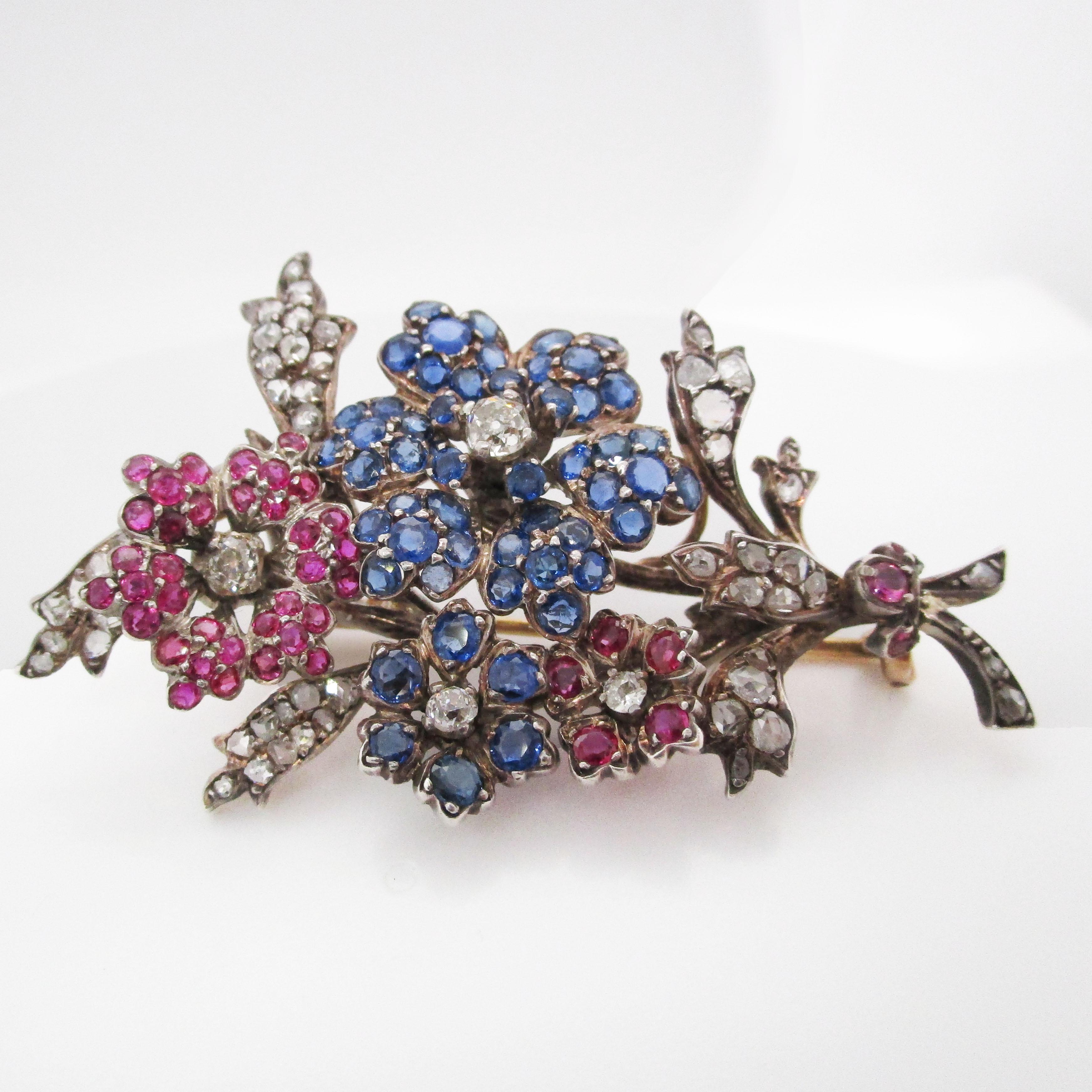 This absolutely enchanting brooch features a jaw-dropping combination of rubies, diamonds, and sapphires set into silver on 14k gold in a gorgeous Victorian brooch from 1880. The layout of the brooch creates the illusion of a dimensional bouquet