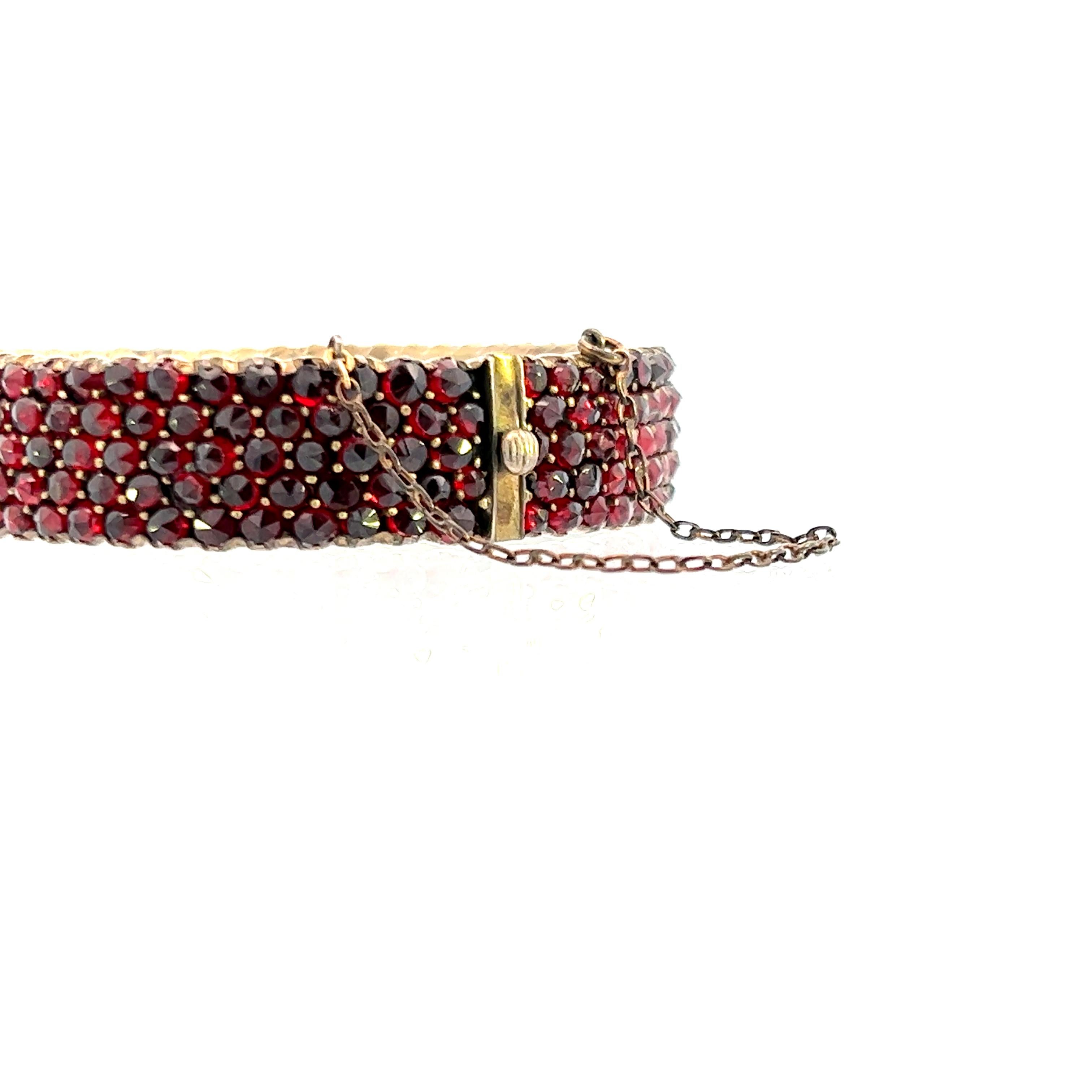 This 1880 Victorian bangle bracelet is gold filled and covered in beautiful garnet. The bangle contains 279 round cut garnets around the full exterior of the bracelet, except for the clasp. The bangle also has a a chain connecting both ends of the