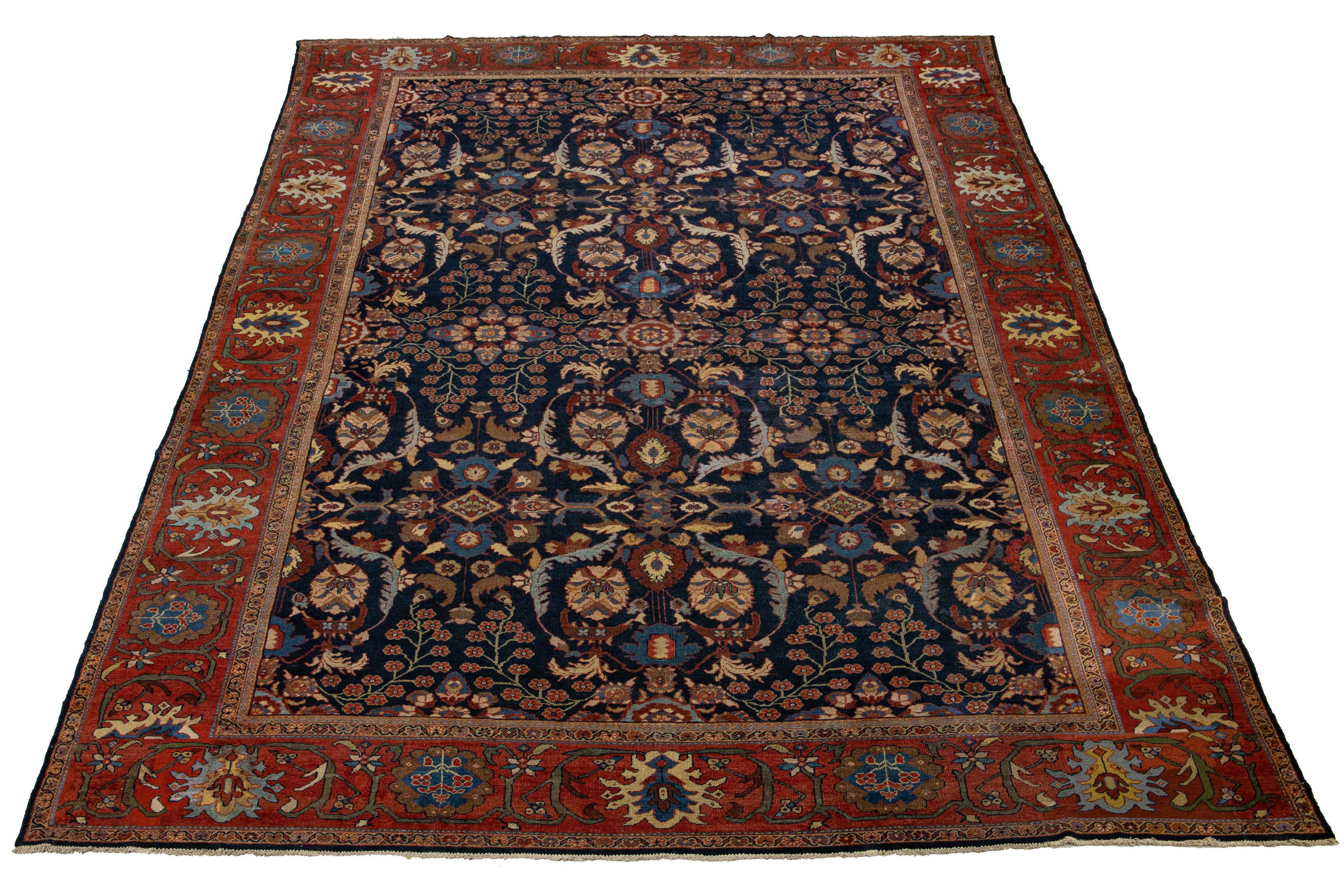 Ce tapis ancien en laine Sultanabad des années 1880 présente un champ bleu marine avec des accents multicolores dans un motif floral all-over, caractéristique des tapis persans. La qualité durable de ce modèle de tapis classique est soulignée par
