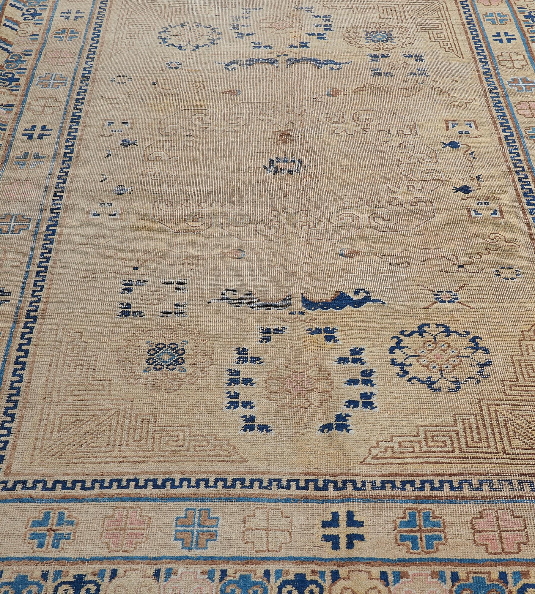 This antique Samarkand Khotan rug from East Turkistan, circa 1880, has faded-gold field with a large hooked shaded aubergine medallion surrounded by indigo blue rosettes, cloud motifs and auspicious symbols, a shaded aubergine key-pattern spandrel