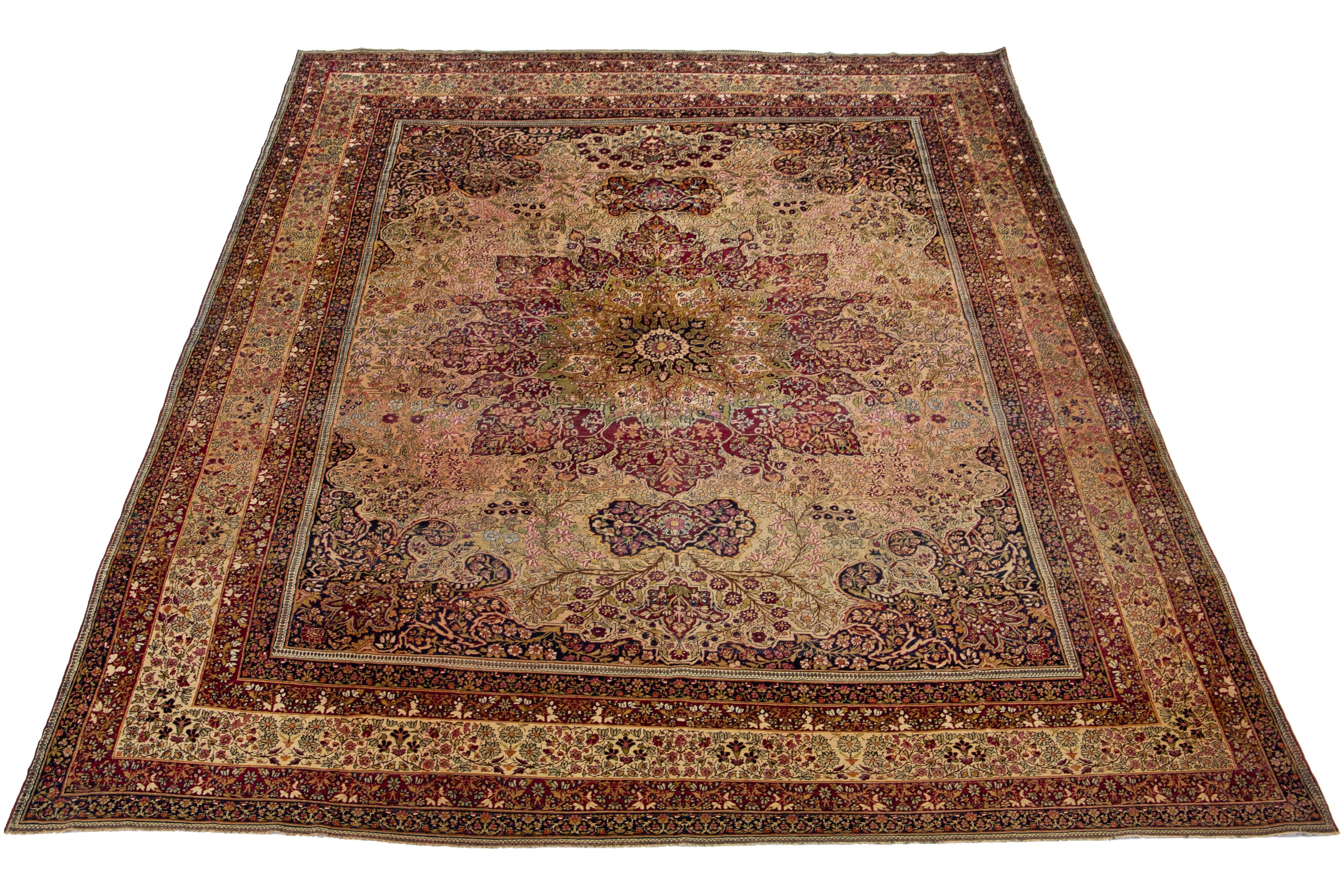This Persian Kerman wool rug from the late 19th century showcases a meticulously crafted allover floral design in peach, green, and goldenrod. This antique rug features a raspberry red field.

This rug measures 9'8