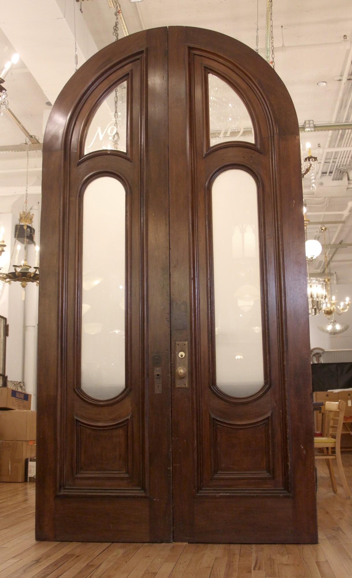 Set of large 1880s antique exterior brownstone doors with two oval frosted glass panes in the middle and two smaller clear glass arched panes on top. The top arched glass panes have No. 113 on them. These walnut doors are original to a NYC