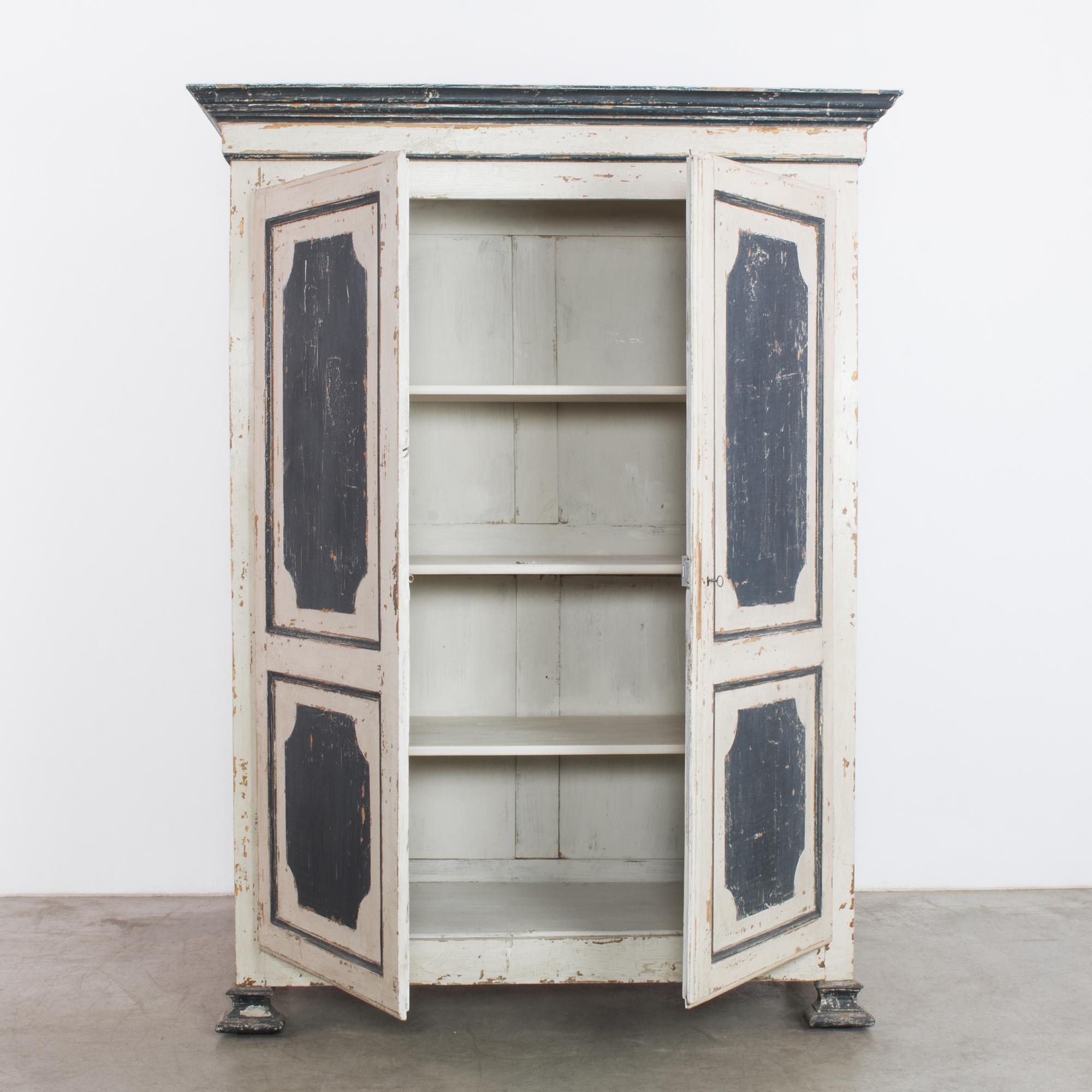 A wooden armoire from Belgium, circa 1880, painted bone white with coal black accents on the panels, top rail and feet. Tall doors open onto a shelved interior. The painted surface has weathered and chipped into a nostalgic patina, misting the