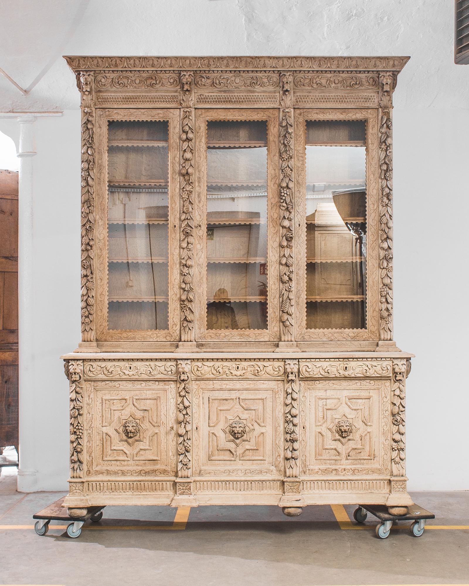 This bleached oak cabinet from 1880, France is composed of a tall vitrine and a large three doors buffet. The stately frame is decorated with extravagant engravings of a variety of grotesque figures, as exotic fruits or lion heads. A scalloped frame