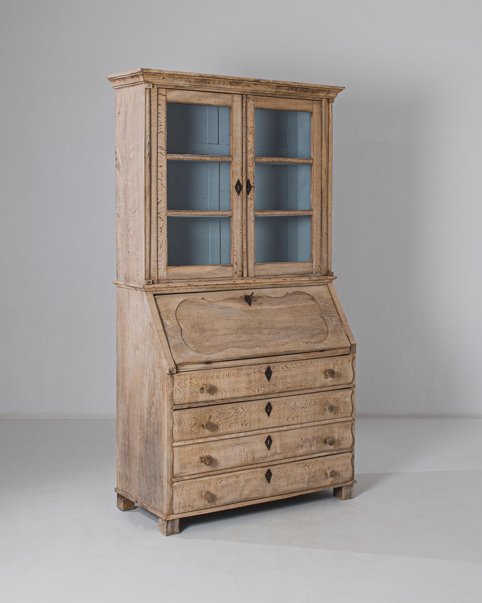 This bleached oak secretary desk and vitrine was made in Belgium, circa 1880. The calming sky blue interior of the upper vitrine complements the rustic tone of the wood, meticulously finished in our atelier. The contoured paneling of the slanted