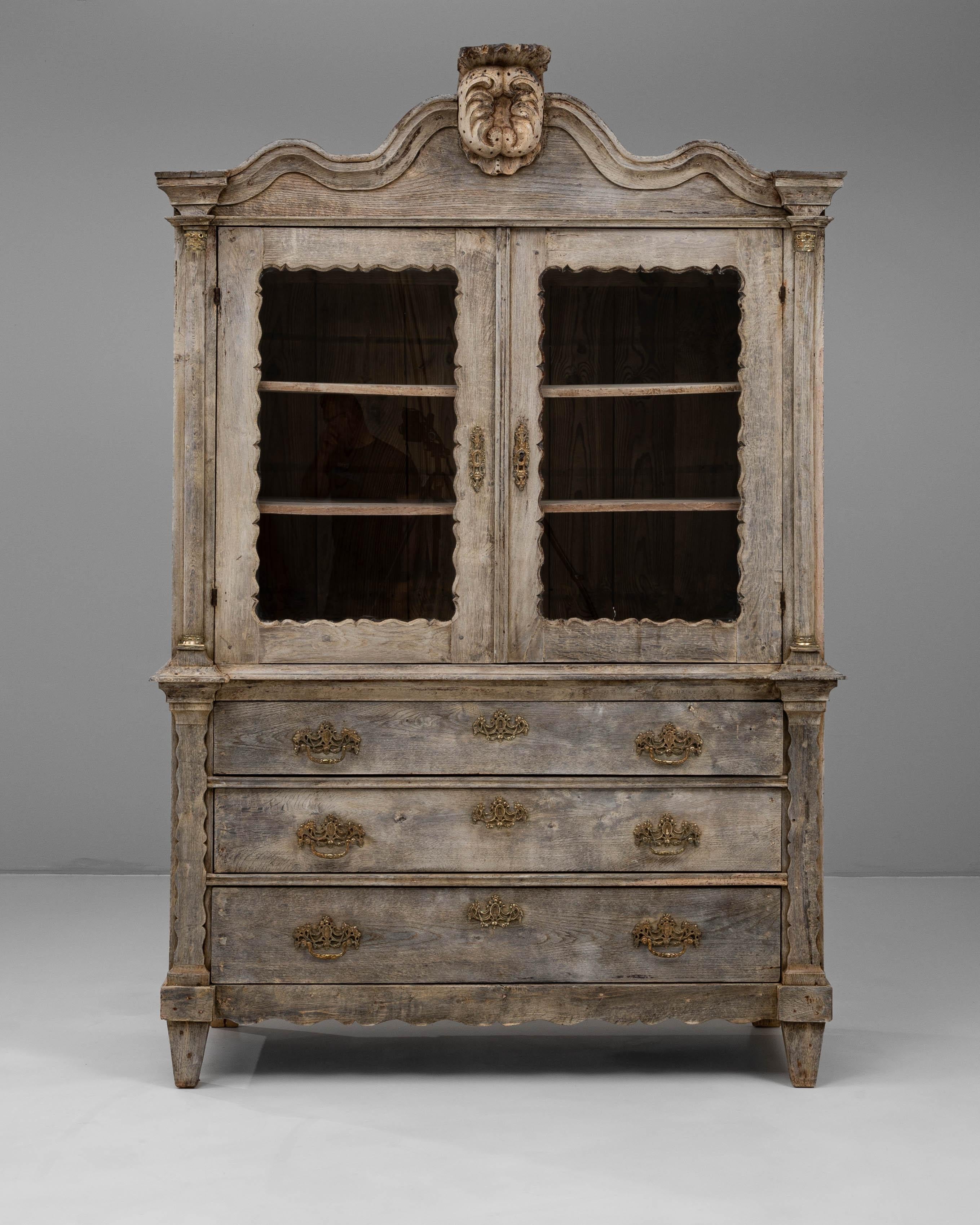 This 1880s Belgian Louis XVI-style oak vitrine exemplifies refined craftsmanship with its elegant proportions and richly detailed ornamentation. The upper section features glass-paneled doors framed by scalloped edges, ideal for displaying fine