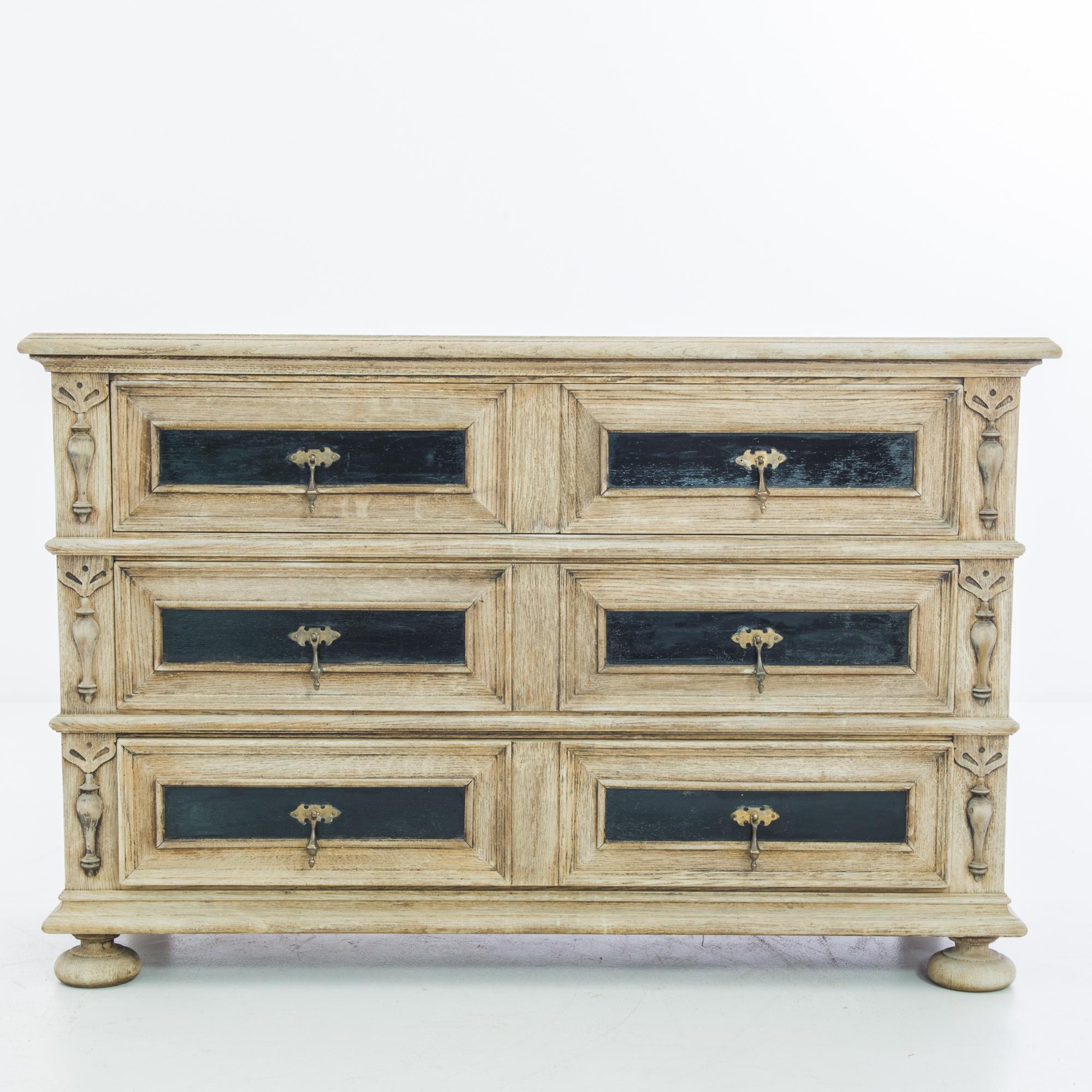 A chest of drawers from Belgium, circa 1880, with a striking monochromatic color palette. The Neoclassical silhouette is embellished with stately carvings: wide bun feet give an impression of solidity and poise. The pale finish of the restored oak