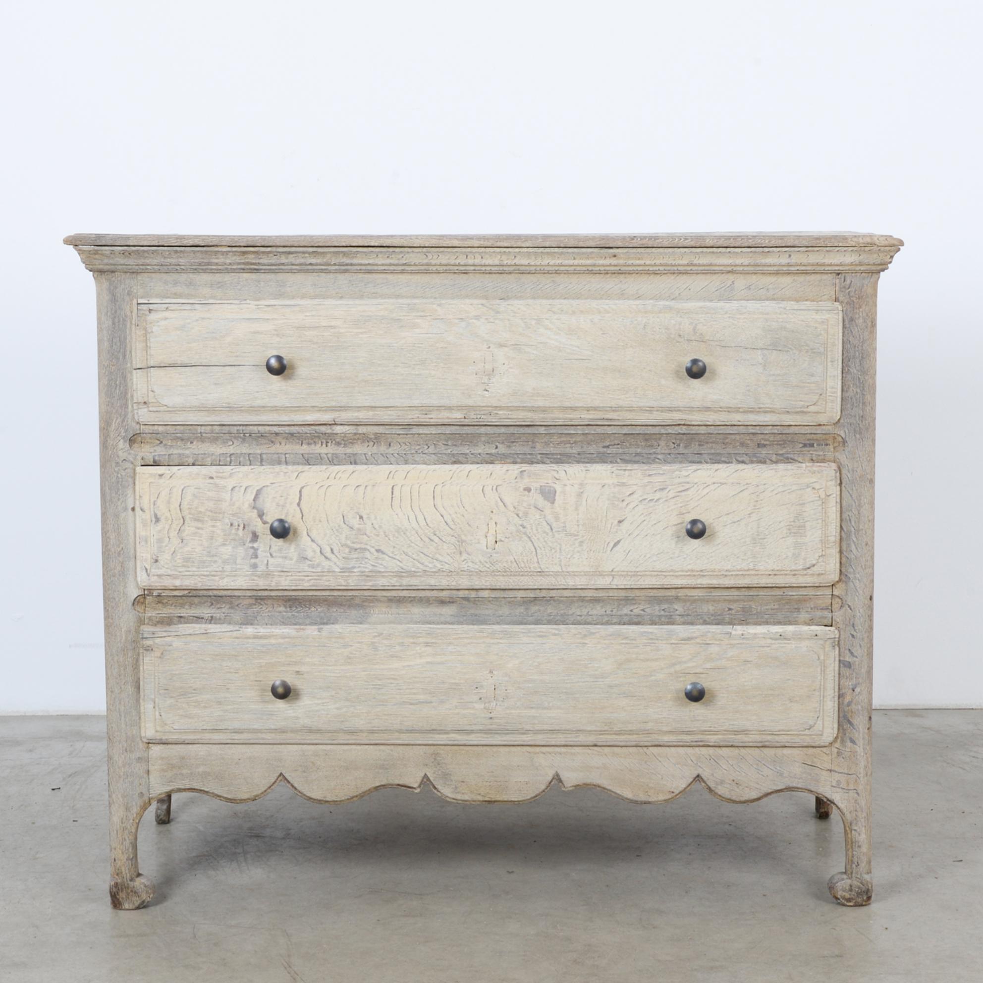 This bleached oak chest of drawers was made in France, circa 1880. It houses three drawers, each with two circular pulls. Four legs with rounded feet elevate the chest, which features a scalloped apron. The finish shows off the distinctive wood