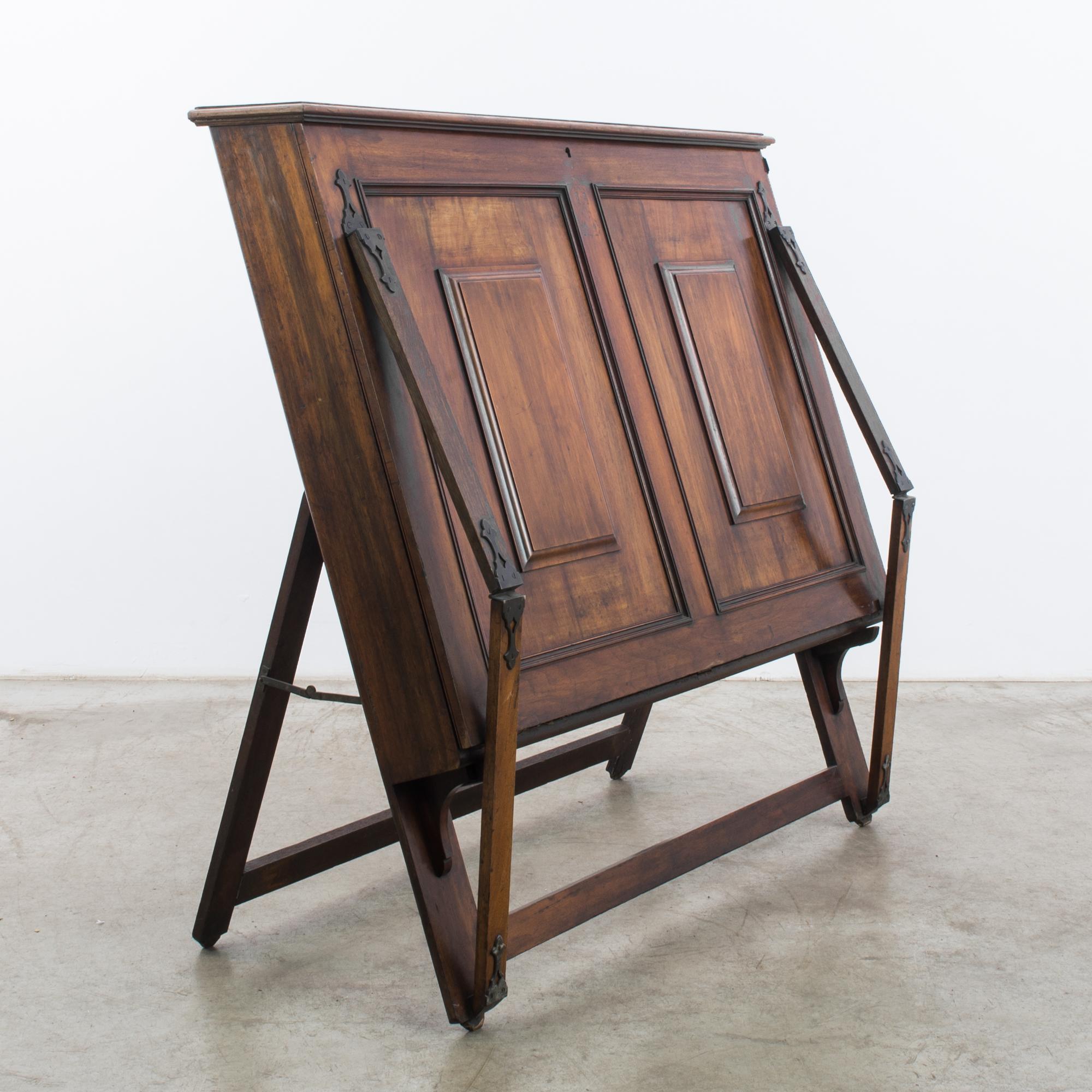 An antique architect’s cabinet from the UK, circa 1880, originally used to store and display large scale drawings and plans. The wood is a dark sienna, with a deep, rich polish. The handsome paneled casing opens out on hinged legs into a low display