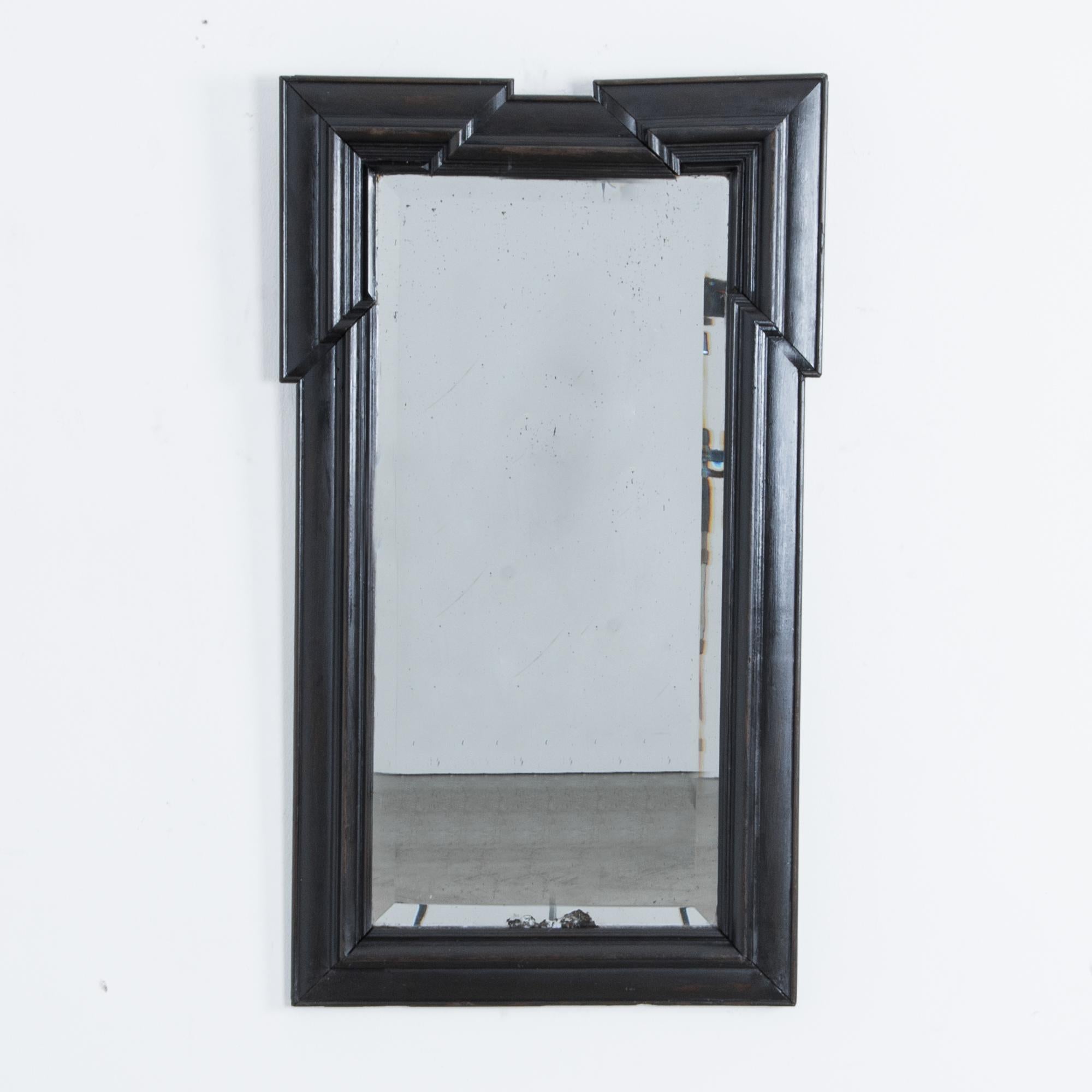 This wall mirror from France, circa 1880, has a black painted wooden frame. A rectangular shape with elegant moldings is dramatically enhanced by the amplified corners of the top of the frame. The bevelled edges of the mirror complement the striking