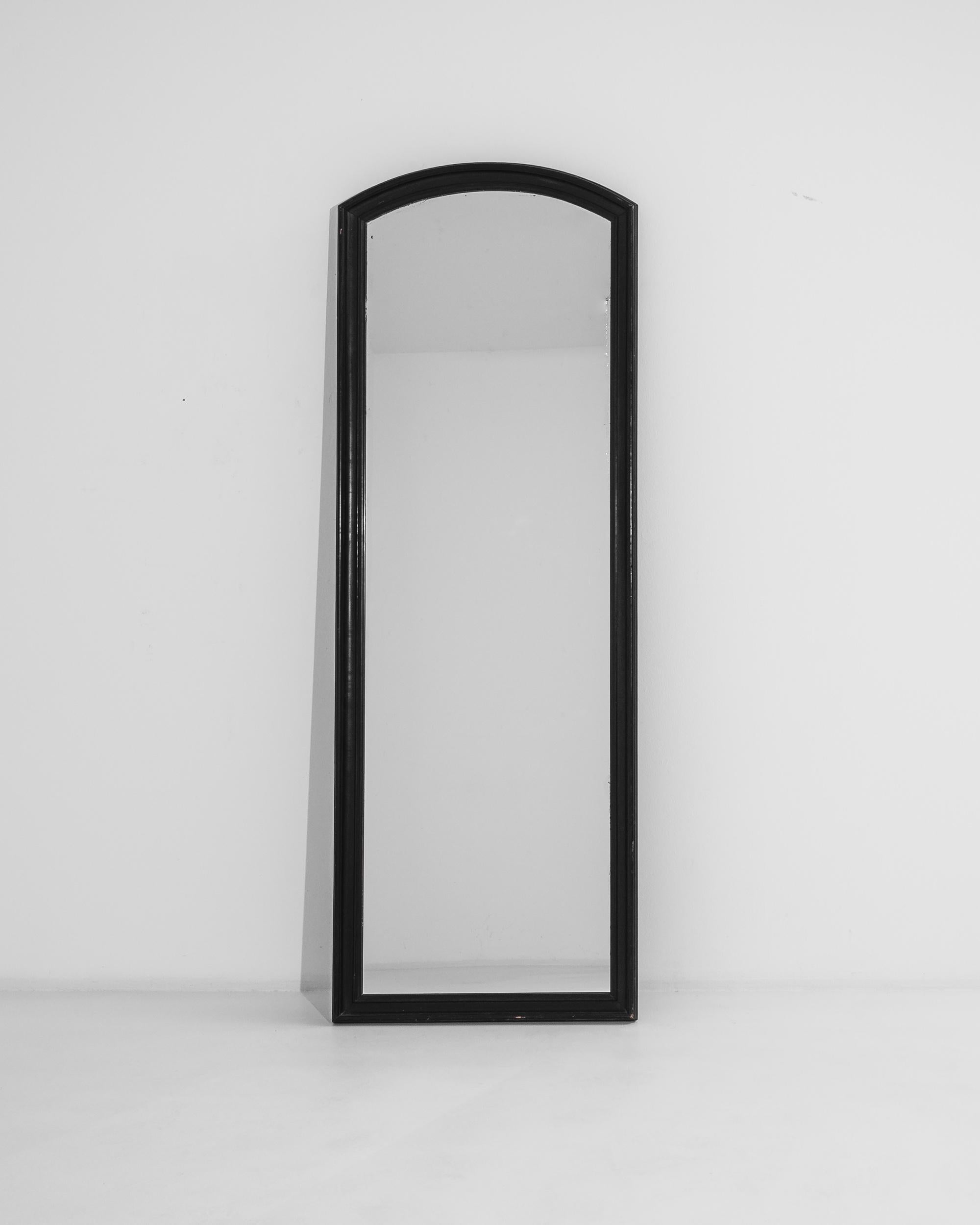 This antique wooden mirror was produced in France, circa 1880. Standing at over six feet, this tall patinated mirror is a sedate, functional statement piece that imparts an elegant simplicity. Slightly patinated, the lustrous black paint reveals