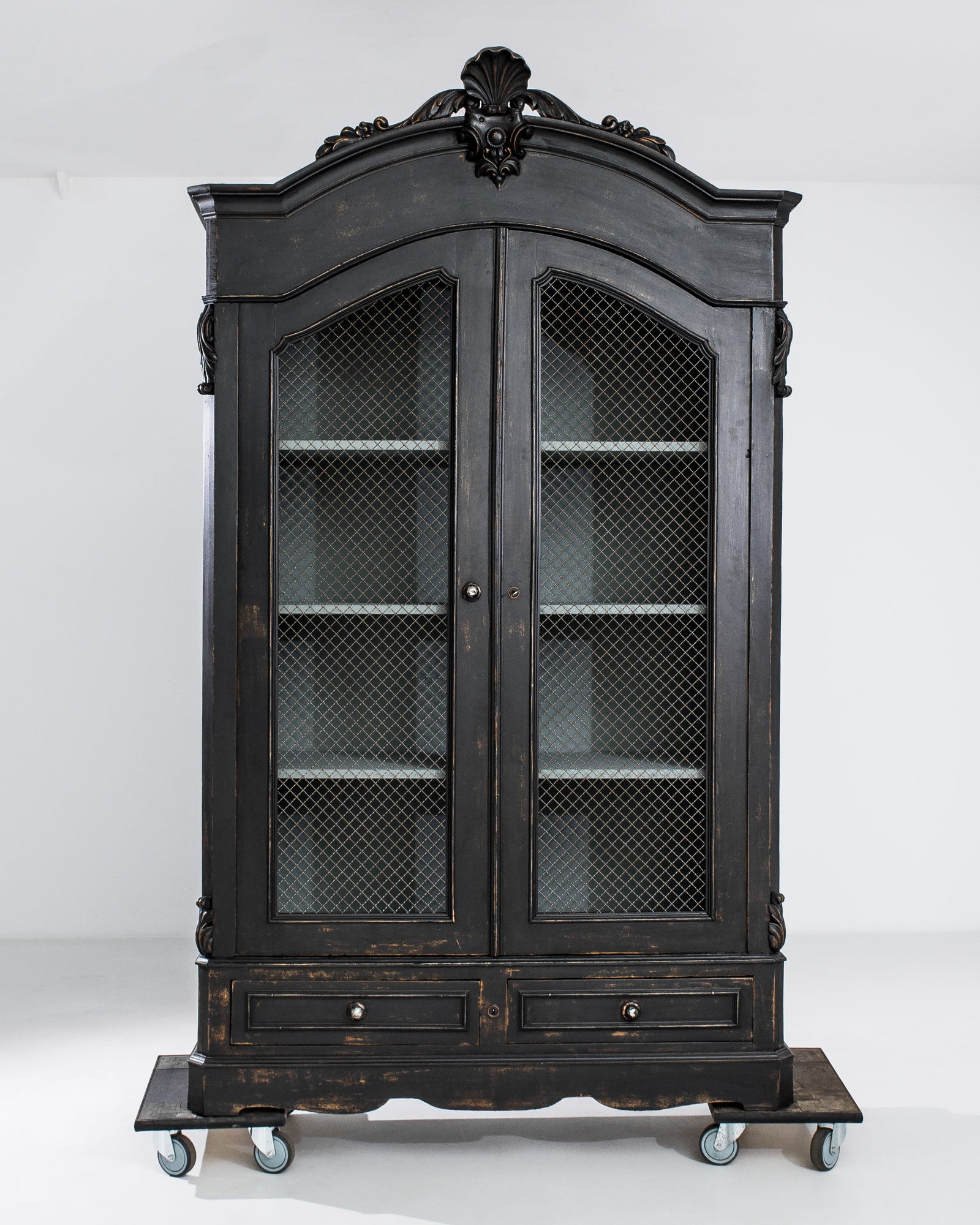 A baroque influenced silhouette and midnight black finish give this antique wooden cabinet a somber, striking presence. Made in France in the 1880s, the wire mesh covering the panels of the doors indicate that the cabinet would have originally been