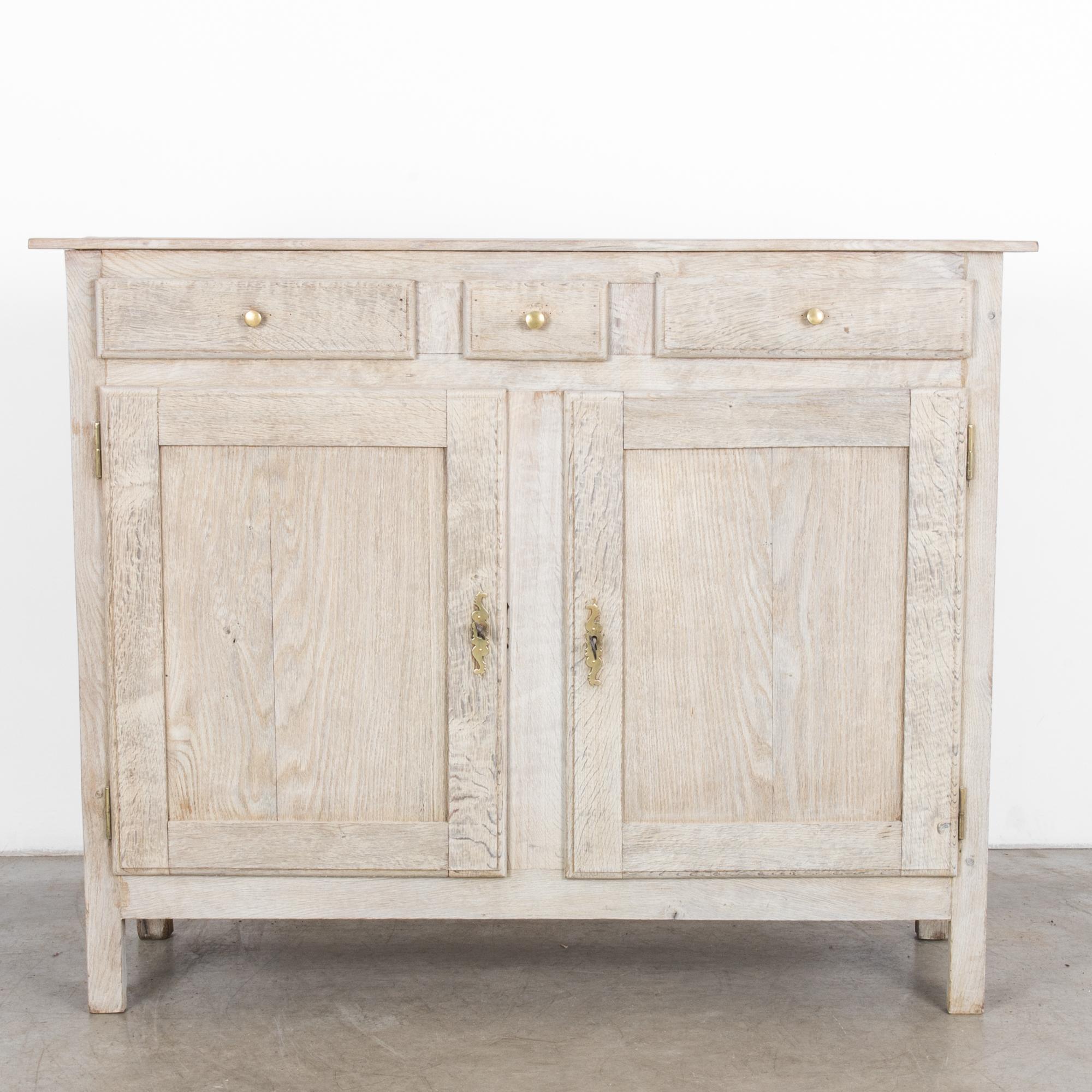 This bleached oak buffet was made in France, circa 1880. The angular legs and rectilinear paneling construct its geometric form, which is embellished by the circular drawer pulls and decorative locks. Double doors below open to reveal two shelves.