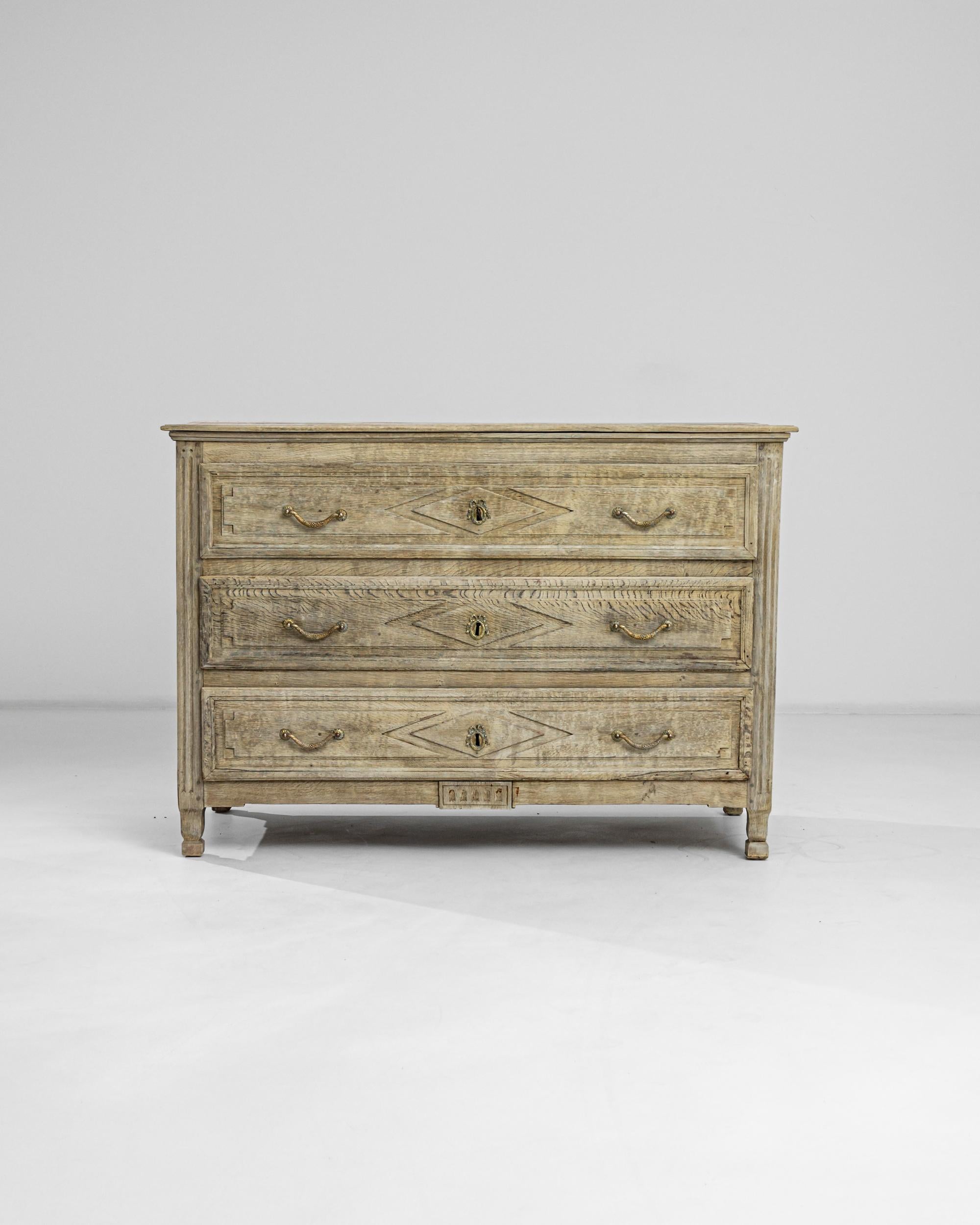 A French bleached oak chest of drawers crafted in the 1880s. This dresser comprises three long drawers fitted with leaf and ribbon-patterned brass handles, offering a wealth of storage space. A revitalizing bleaching process has allowed its details