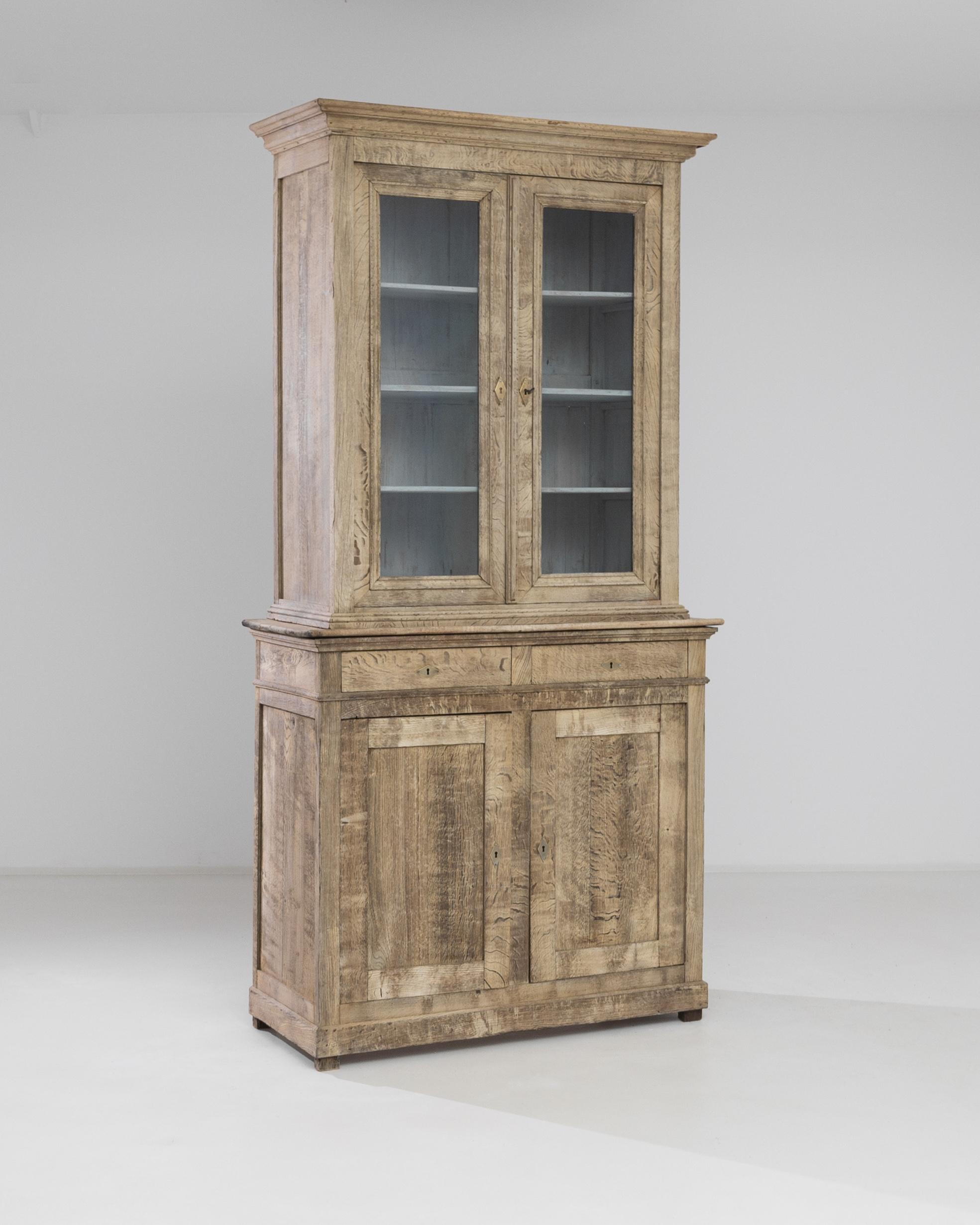 This antique vitrine has been crafted in France, circa 1880. Standing on discrete block feet, this wooden vitrine features a molded top, a four shelves top case, two front drawers and a large two shelves bottom case. The beveled doors are ornamented