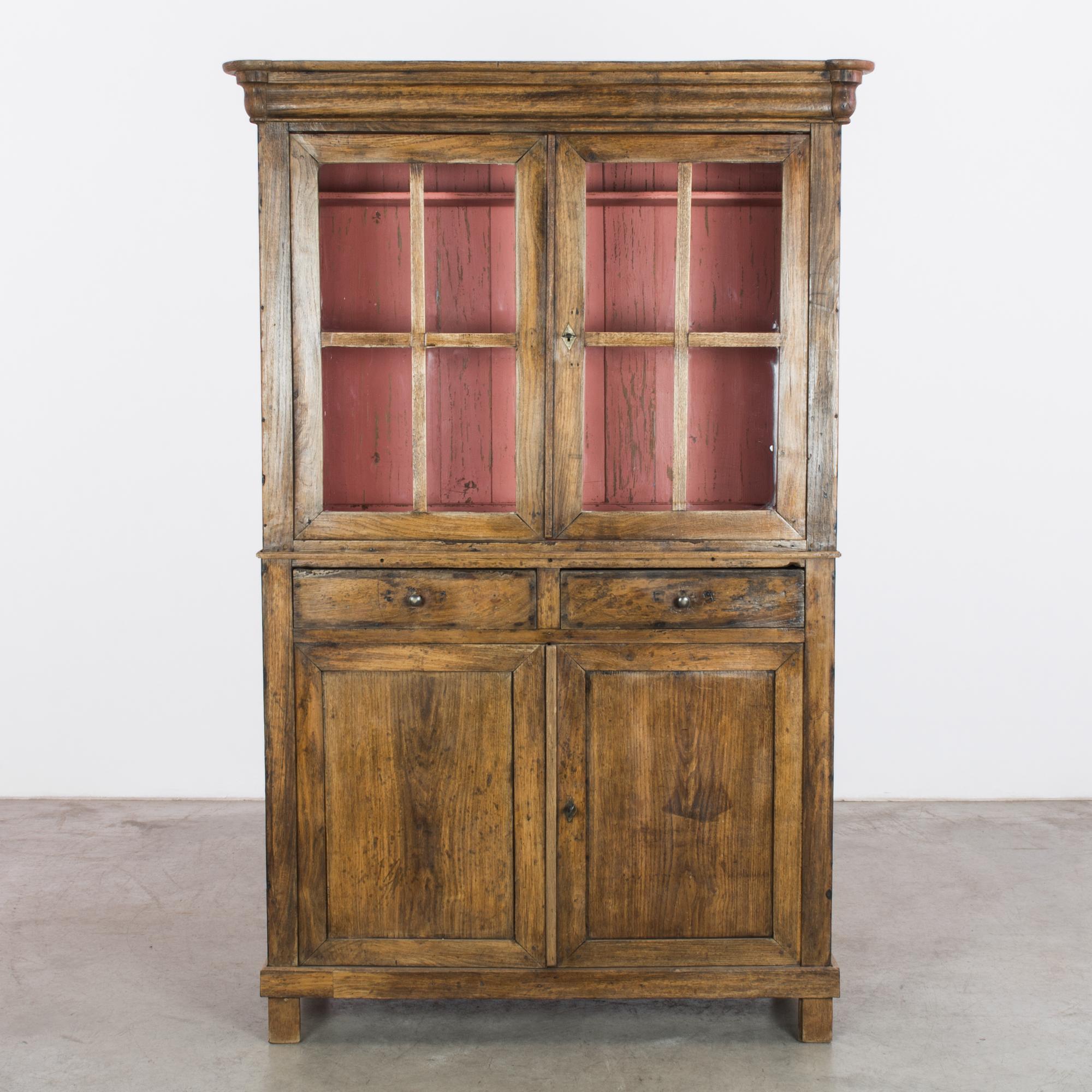 A wooden vitrine from France, circa 1880. A handsome cabinet of polished oak with a lower cupboard, twin drawers and two paned windows which peep onto a rose pink interior. The dusky tone and gentle weathering of the pink paint makes a sweet