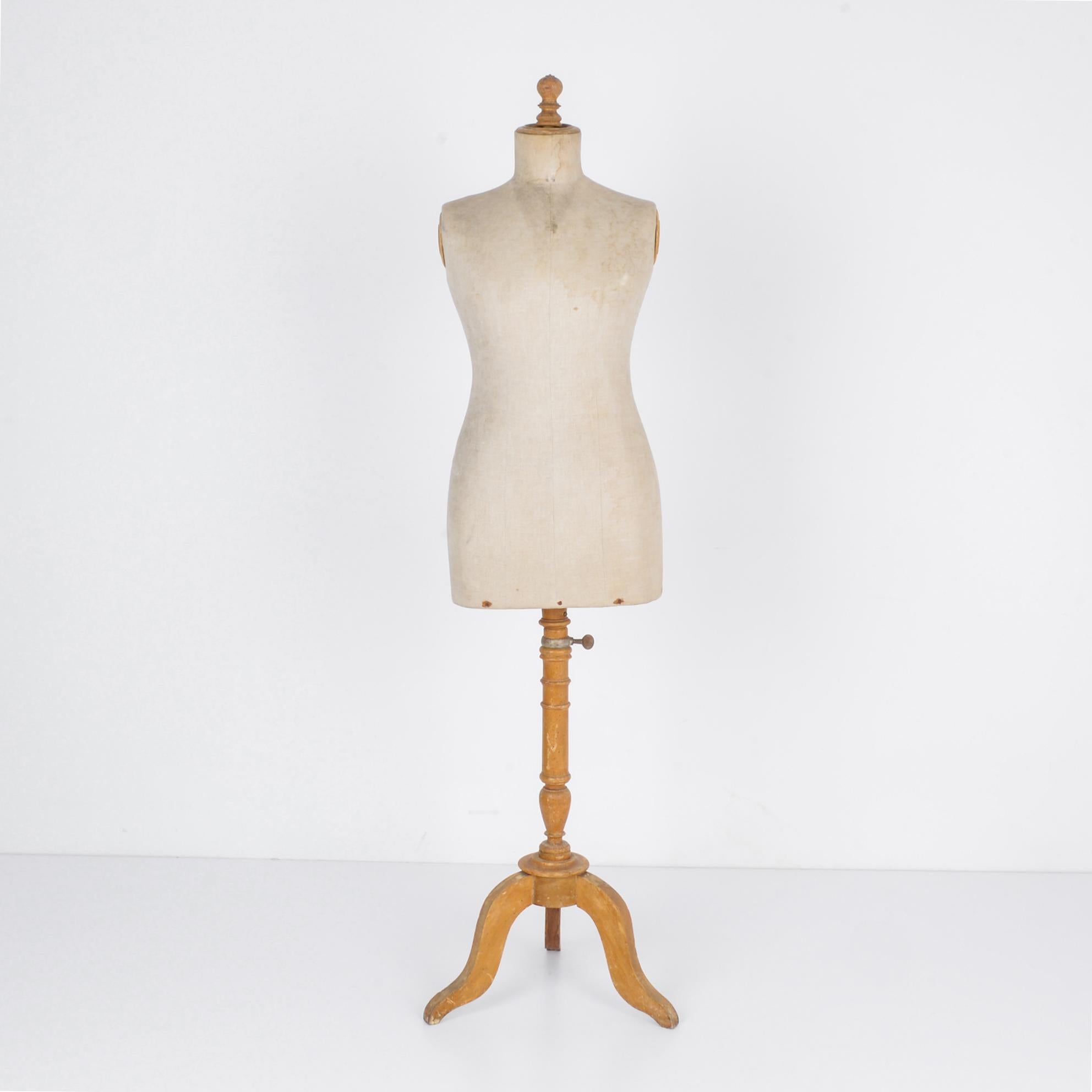 This wooden mannequin was made in France, circa 1880. It has a silhouette of a woman and features a turned stand and tripod base. The body is lined with time-worn linen, recalling the days of elaborate fittings and custom made clothing at a