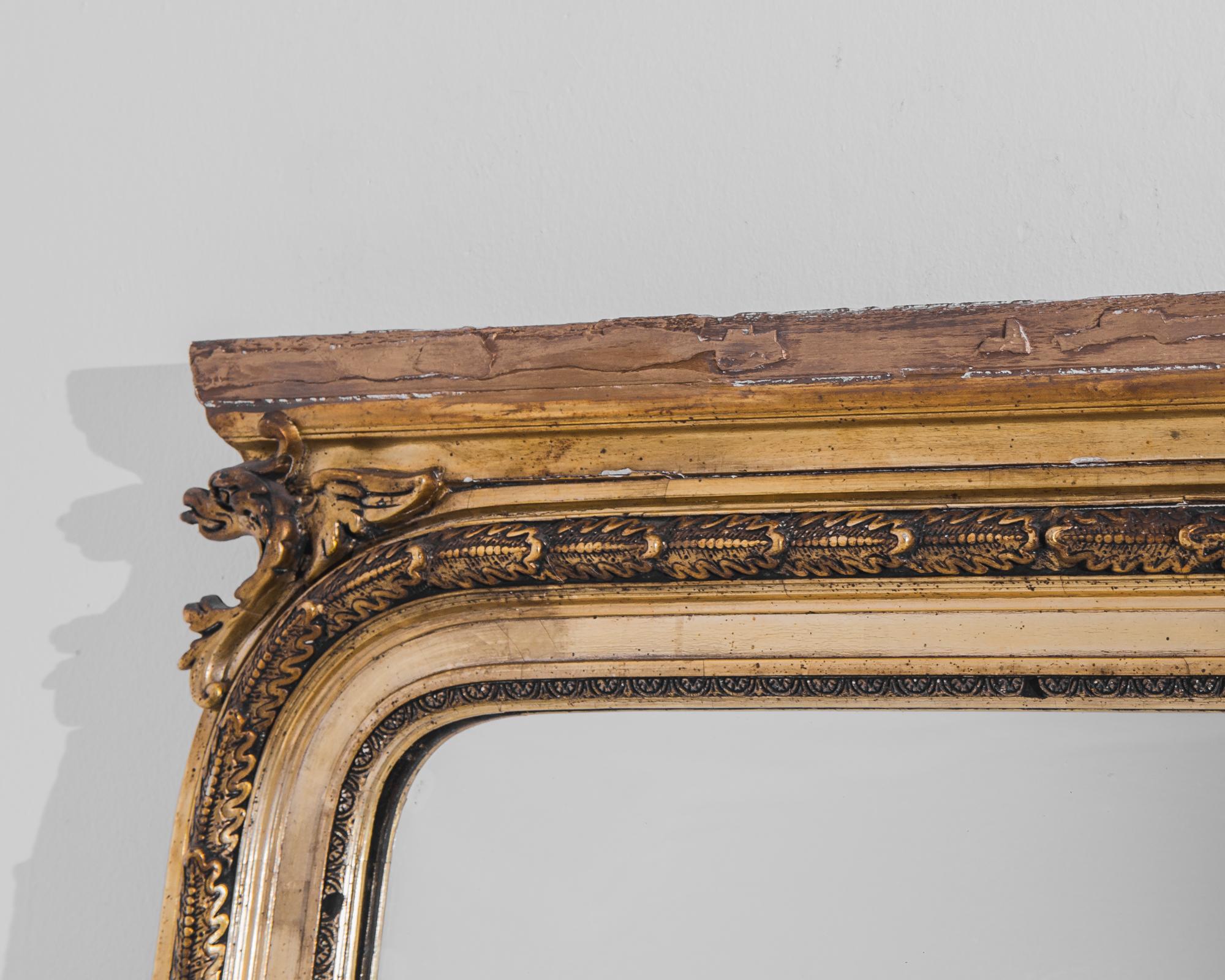 A gilded wood mirror produced in France circa 1880. A richly decorated gilt rim encircles this mighty mirror with a repeating leaf motif and griffin heads emerging from the upper corners. Beautifully carved and tall enough to see your whole outfit,