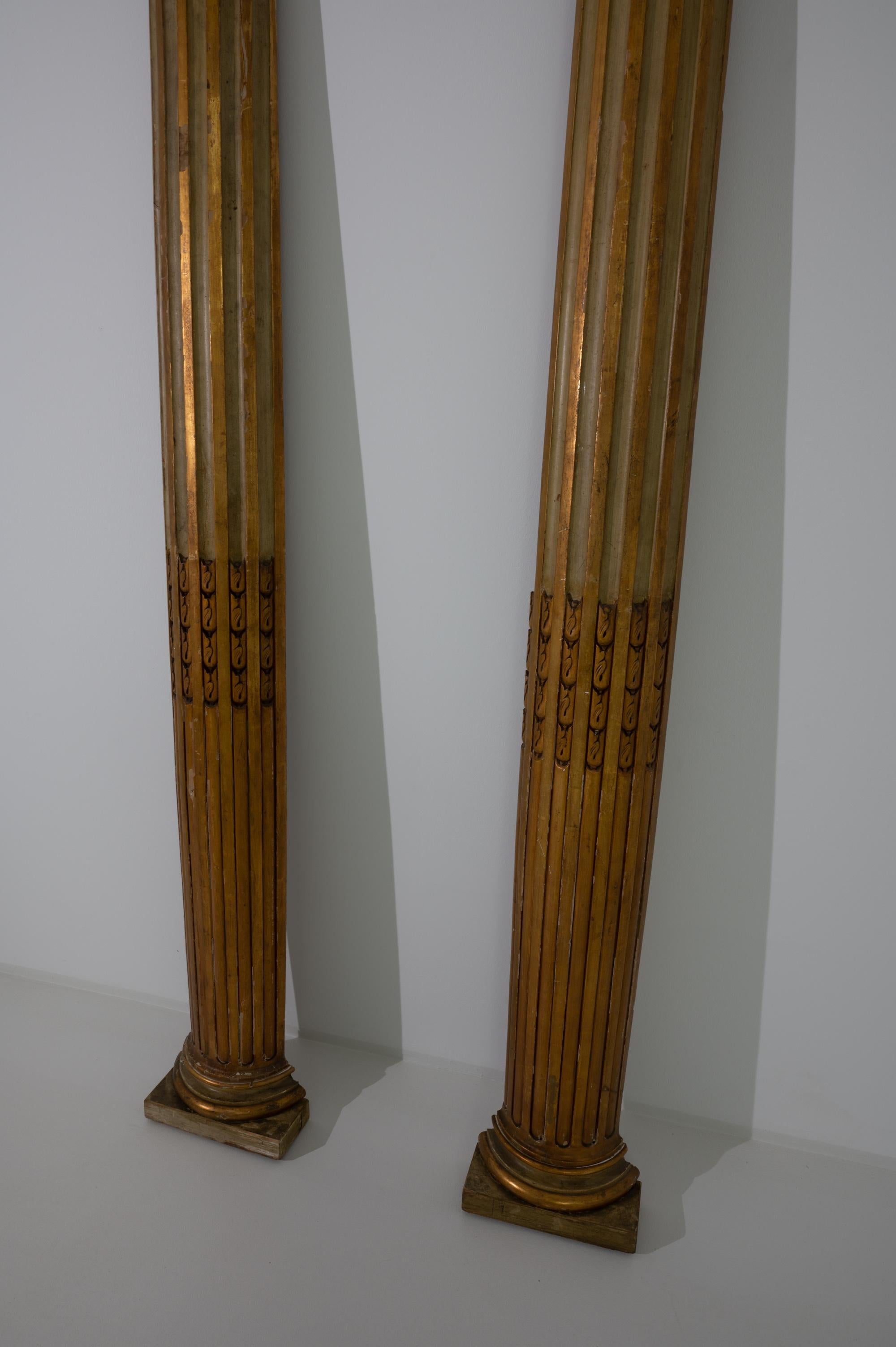 This pair of antique wooden columns was produced in France, circa 1880. Crowned by carved scrolls and adorned with fluted moldings, these two tall columns take on a corinthian inspiration. Elevated on a discrete base, these regal columns feature two