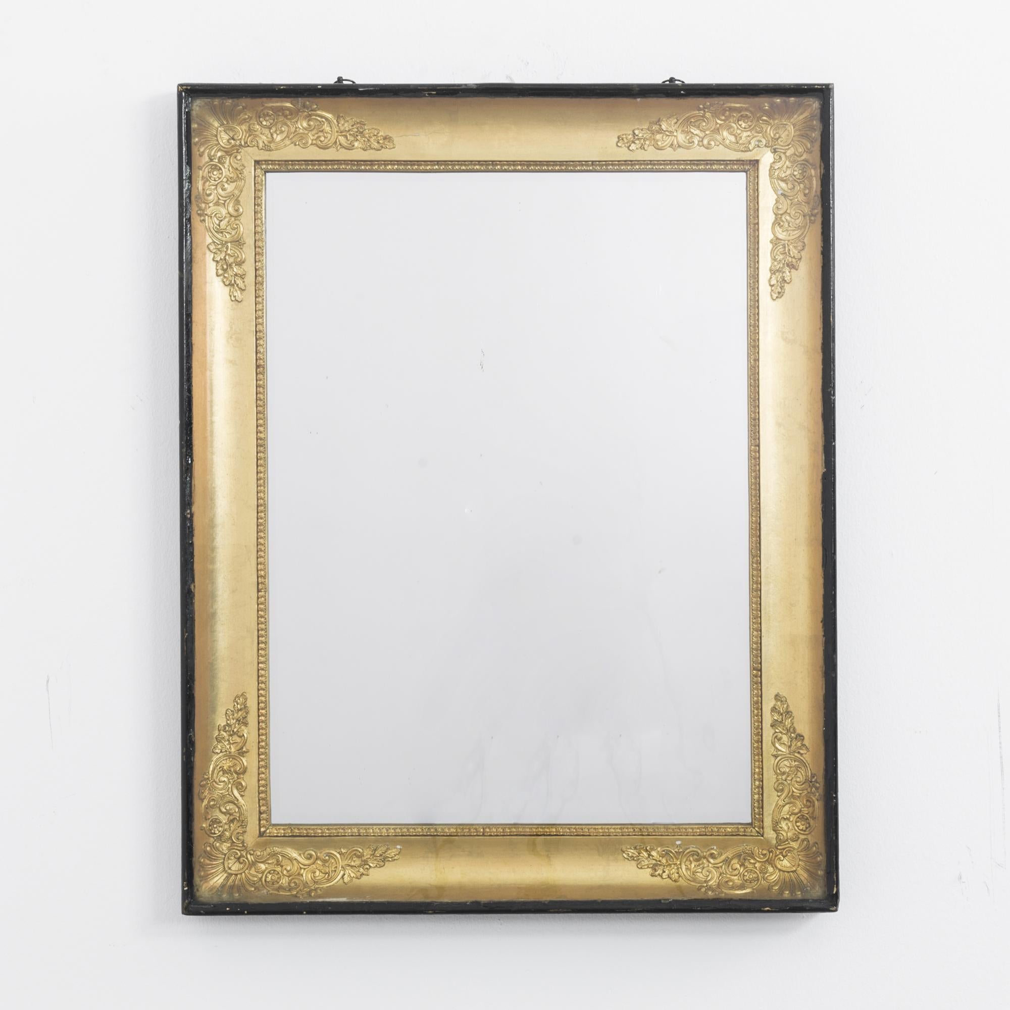 Made in France, circa 1880, this mirror features a decorative wooden frame. The neoclassical influence can be observed in the intricate plaster moldings of foliage, tendrils, and a scallop shell in each corner. A box frame, painted black,