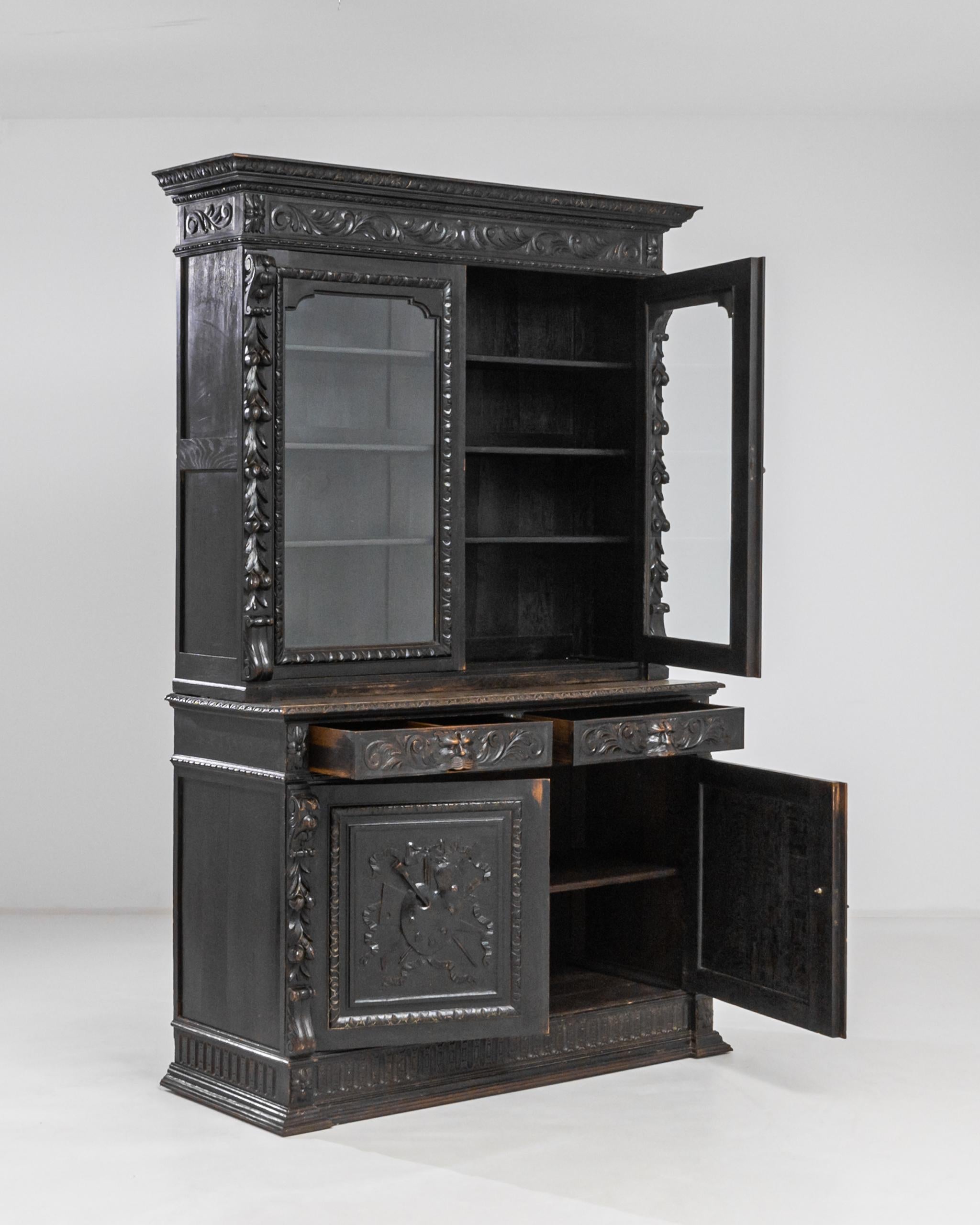 Elaborate Neo-Renaissance carvings and the deep black finish of the wood lend this antique vitrine a powerful presence. Made in 1880s France, a pair of paned windows are framed by carved festoons of leaves, fruit and scrolling acanthuses.