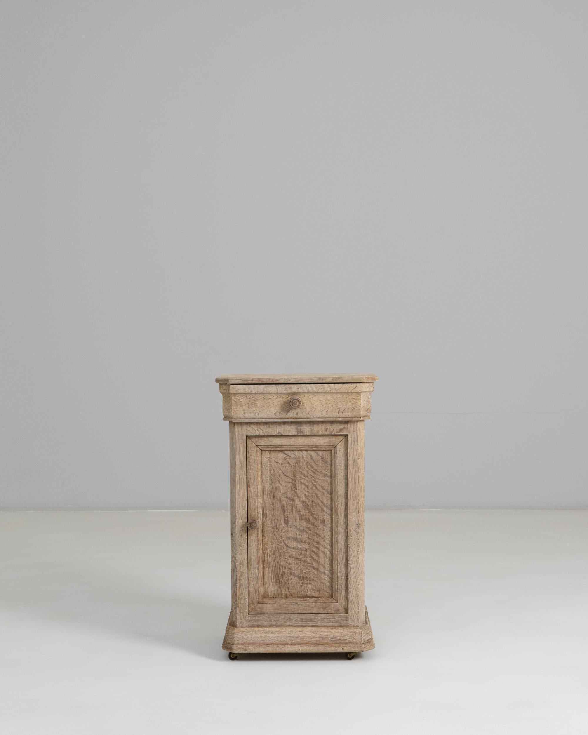This 1880s French oak bedside table showcases the understated refinement of provincial craftsmanship, blending simple lines with the warm texture of aged wood. Its single door and upper drawer are framed by subtly molded panels that highlight the