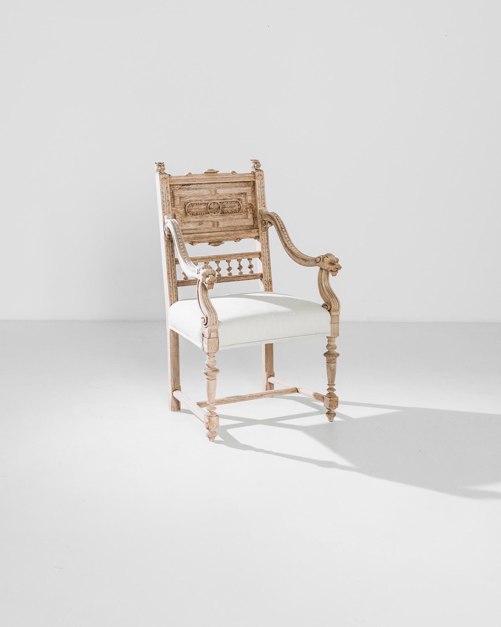 An oak armchair with upholstered seat from France, produced circa 1880. A regal armchair from the late 19th century, featuring an off-white cushion contrasted against richly carved blond wood. A highlight of this chair are the lion’s heads at the