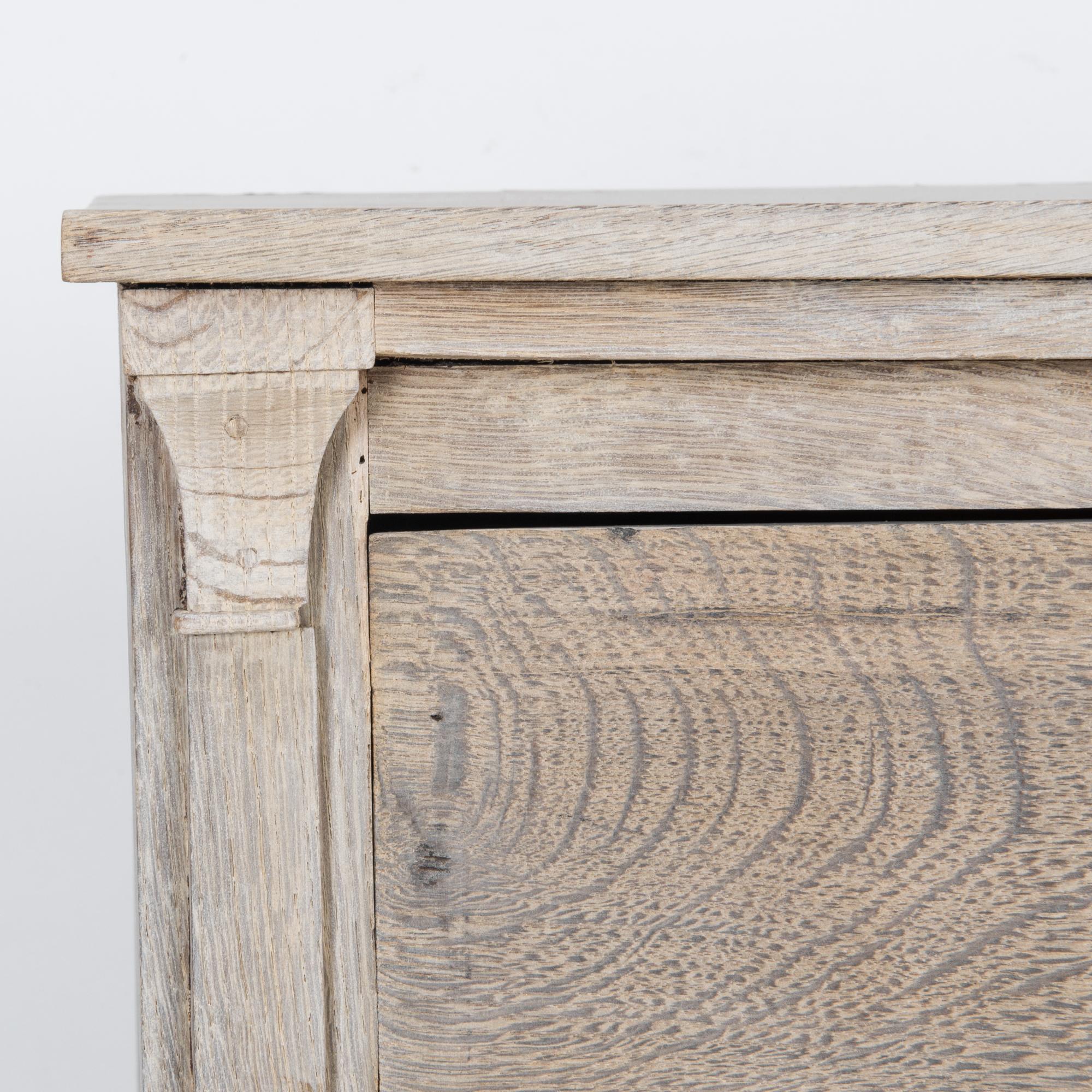 An antique oak chest of drawers from 1880s France. The upright form is enhanced by column moldings which unfold into graceful cornices, a subtle neoclassical accent. A liquid grain floats across the surface of the wood, restored to a pale natural
