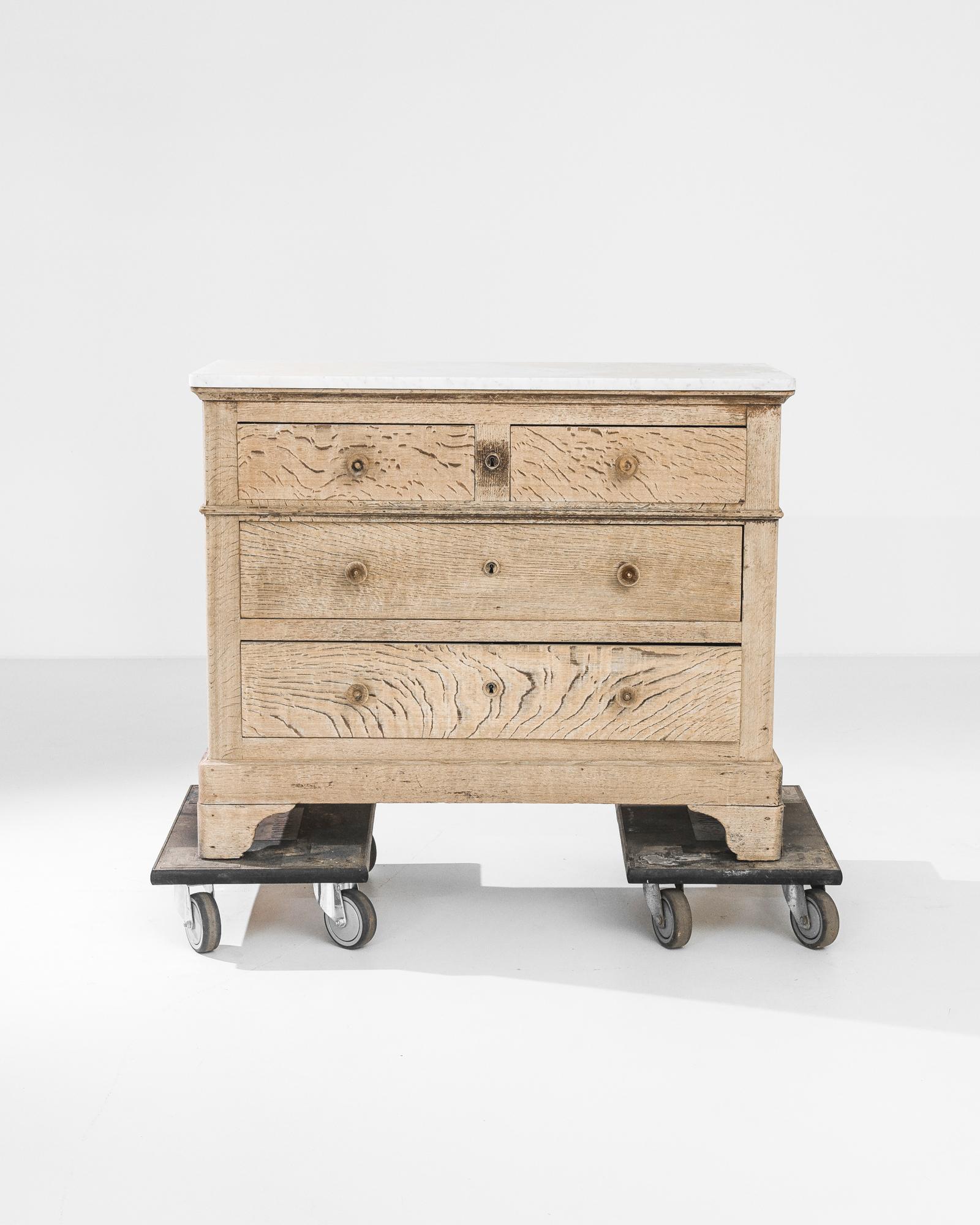 An oak chest of drawers from 1880s France, crowned by a piece of grey veined white marble. A handsome upright silhouette, elevated upon contoured feet. The oak has been restored in our workshops to a natural golden finish, exhibiting a fluid and
