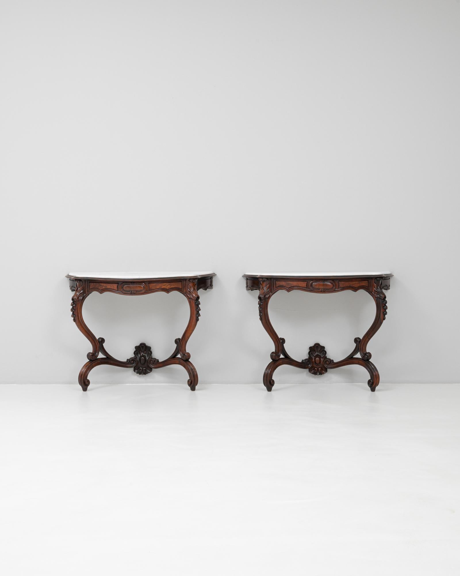Questa coppia di consolle francesi del 1880 esemplifica l'opulenza e la maestria della fine del XIX secolo. Ogni tavolo è realizzato in legno scuro e ricco, ornato da dettagli finemente intagliati a mano che evidenziano foglie d'acanto che scorrono,