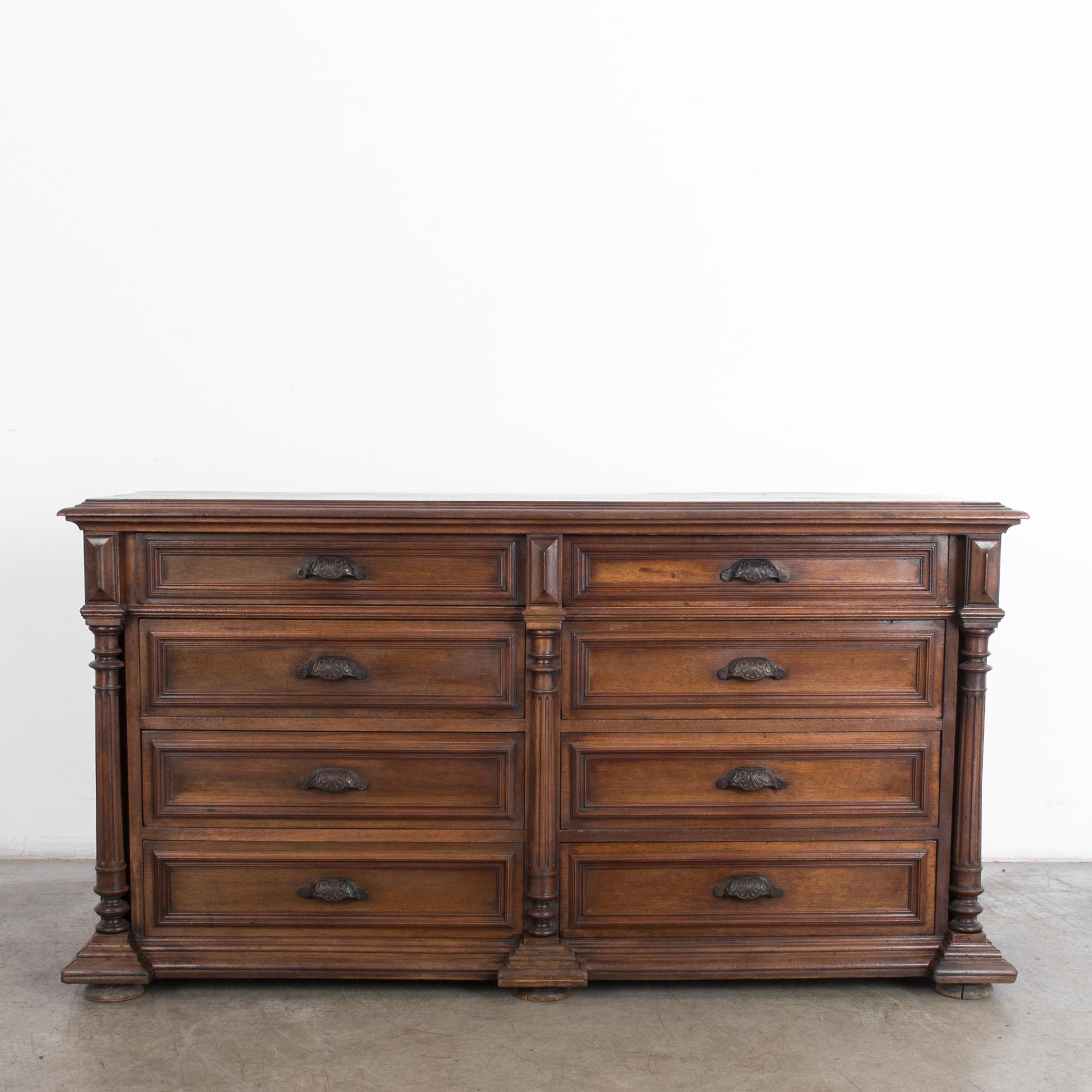 A wooden chest of drawers from France, circa 1880. Eight pullout / pull-out drawers are framed by fluted column moldings. Shell-like curves of the drawer handles provide a gentle counterpoint to the linear neoclassical silhouette. The deep tone and