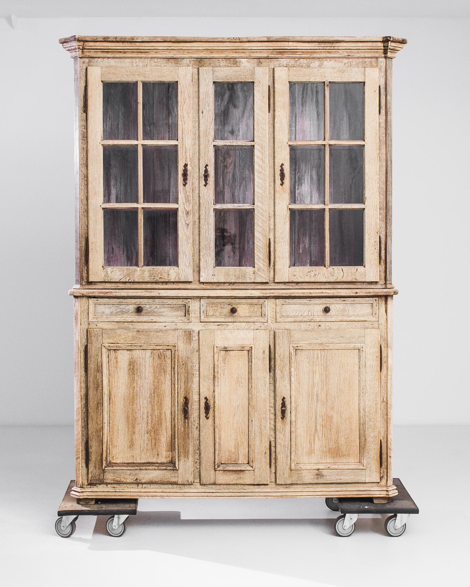 Natural oak and an enigmatic interior patina give this antique vitrine an enticing personality. Made in France in the 1880s, the cabinet has a country aesthetic, with mullioned window panes and paneled cupboards. The pale barley and burnt caramel