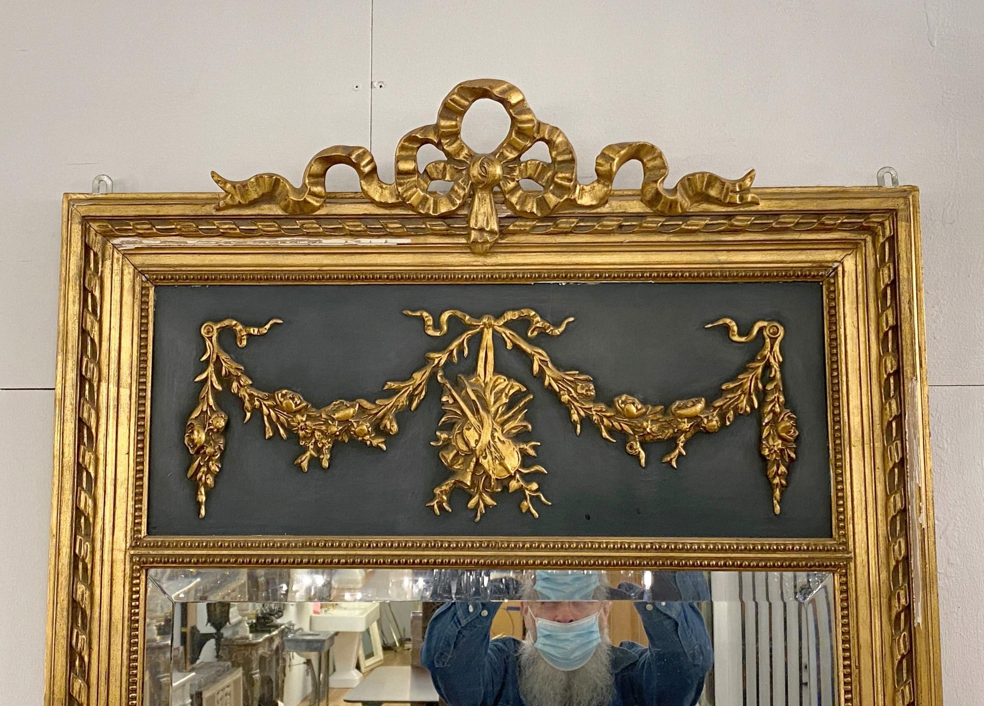 1880s French trumeau mirror with beveled glass and gilded wood, Featuring a ribbon detail on top. The top panel is painted dark green and detailed with a delicate ribbon and violin motif. This can be seen at our 333 West 52nd St location in the
