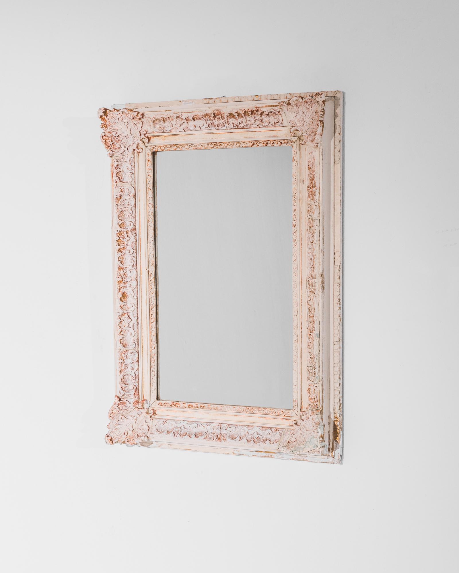 A wooden mirror from 1880s France. Elaborate Rococo carvings decorate the wings of the frame, highlighted by the contrasting tones of the patinated wood. The design of scrolling leaves and the soft, bright color palette, ranging from cream to deep