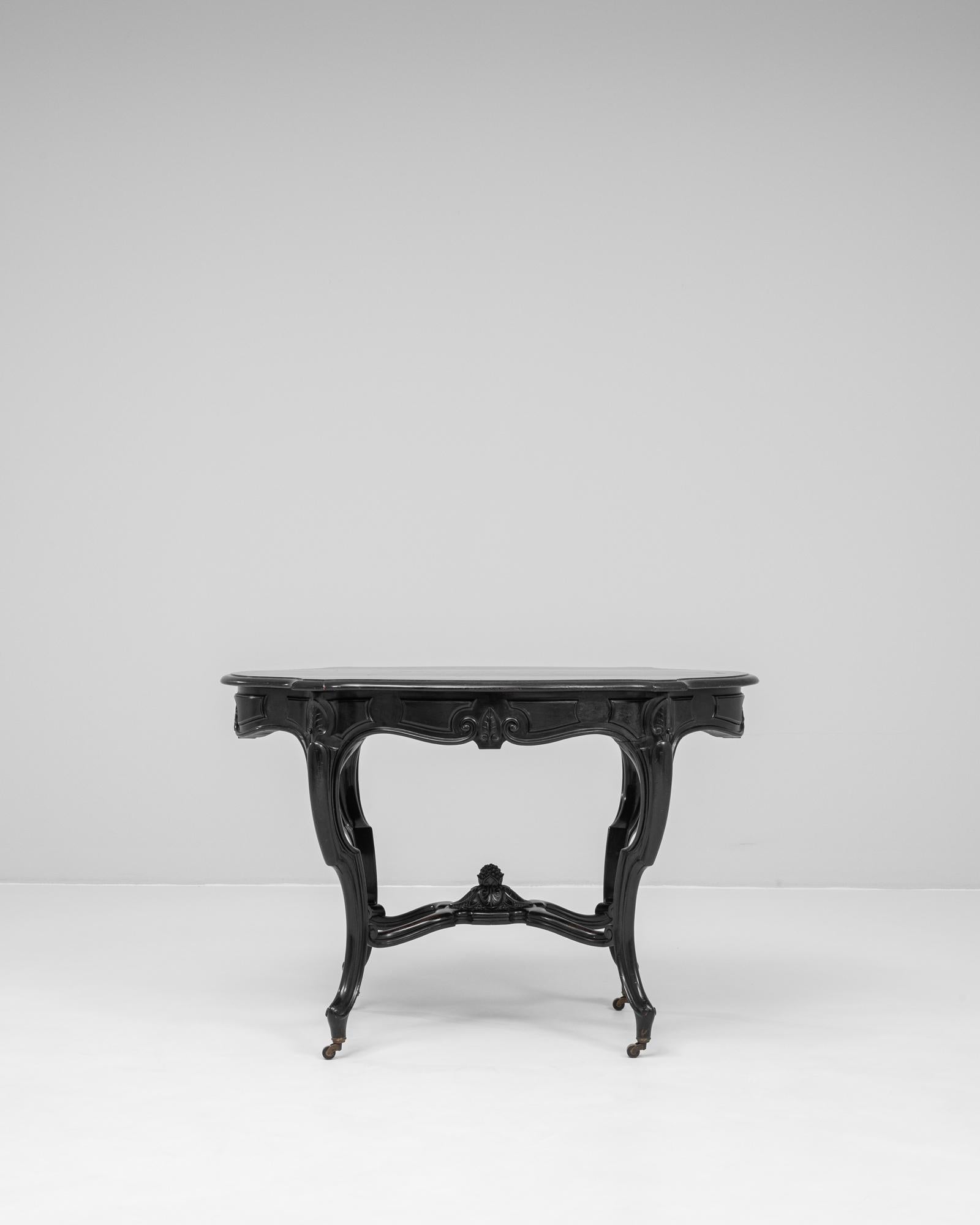 This 1880s French table is a graceful example of late 19th-century craftsmanship, finished in a rich black patina that highlights its sculptural silhouette. The shaped apron features carved floral and scroll motifs, while the cabriole legs and