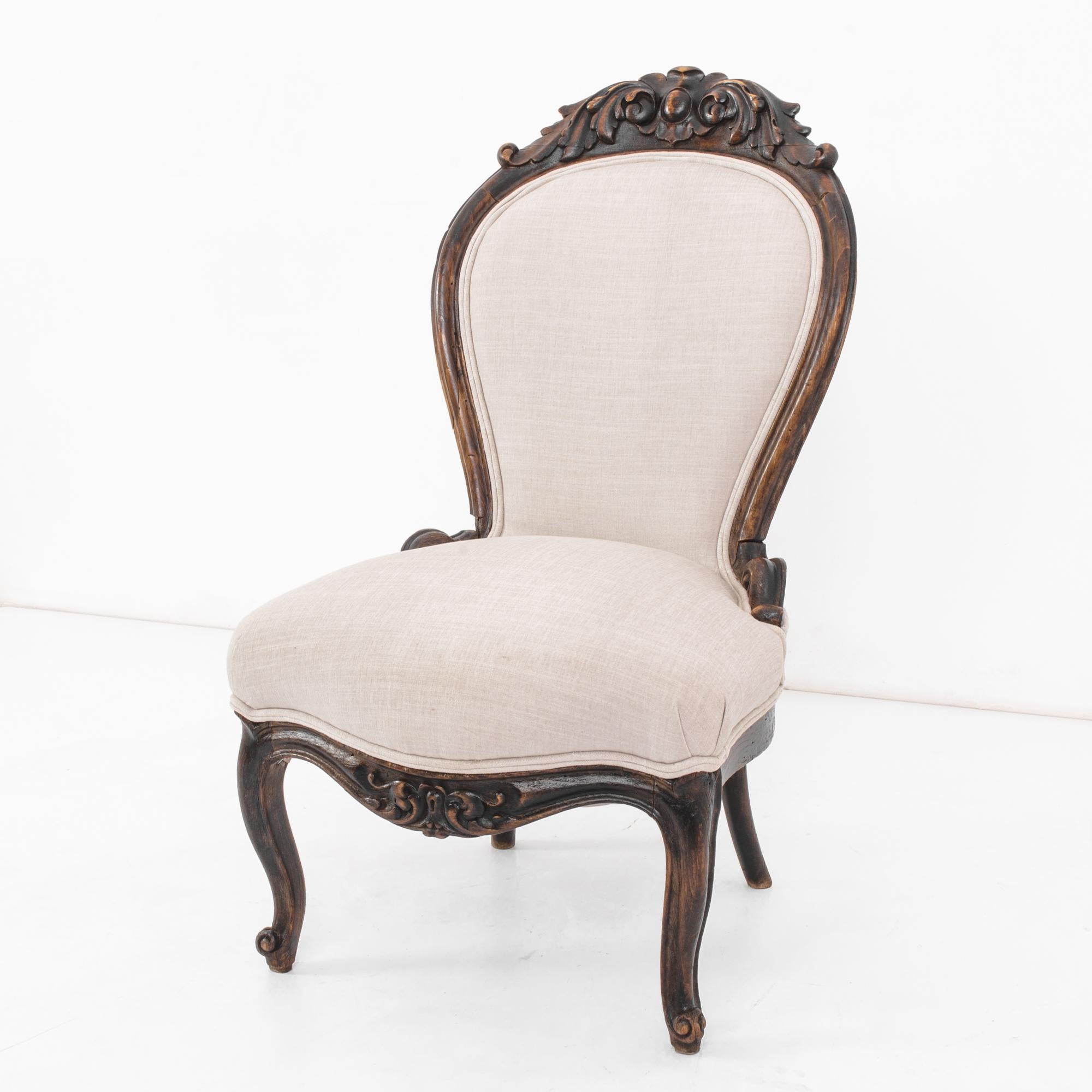 Indulge in the timeless elegance of this 1880s French Wooden Chair. Crafted with exquisite artistry, the dark-finished wood showcases intricate carvings that adorn the beautiful apron and top carved piece. The upholstered seat and back, in a crisp