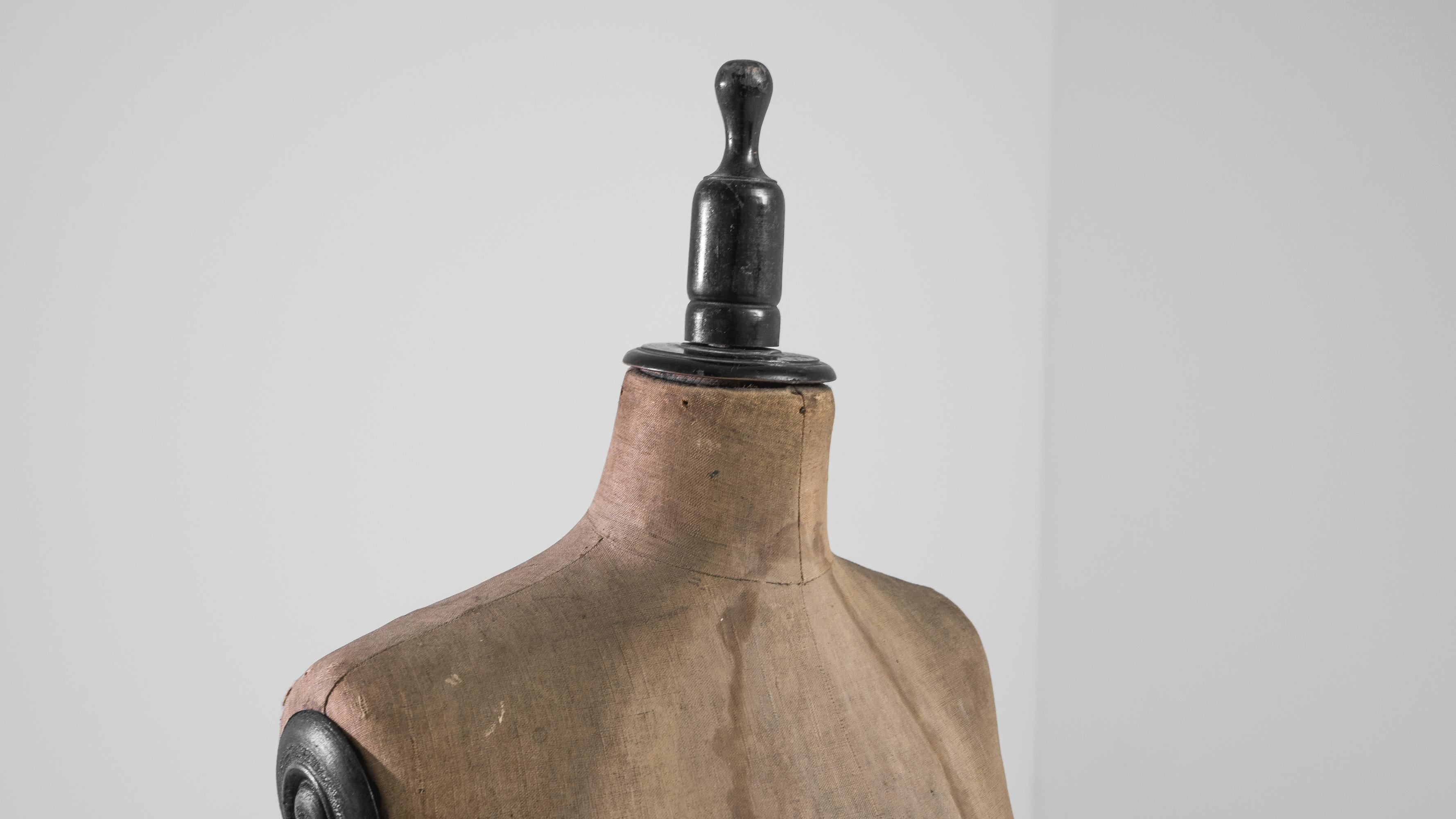 Capture the essence of early 20th-century French craftsmanship with this Antique French Wooden Mannequin. Crafted with precision, this unique piece showcases the silhouette of a woman and stands on a turned stand with a weathered tripod base. The