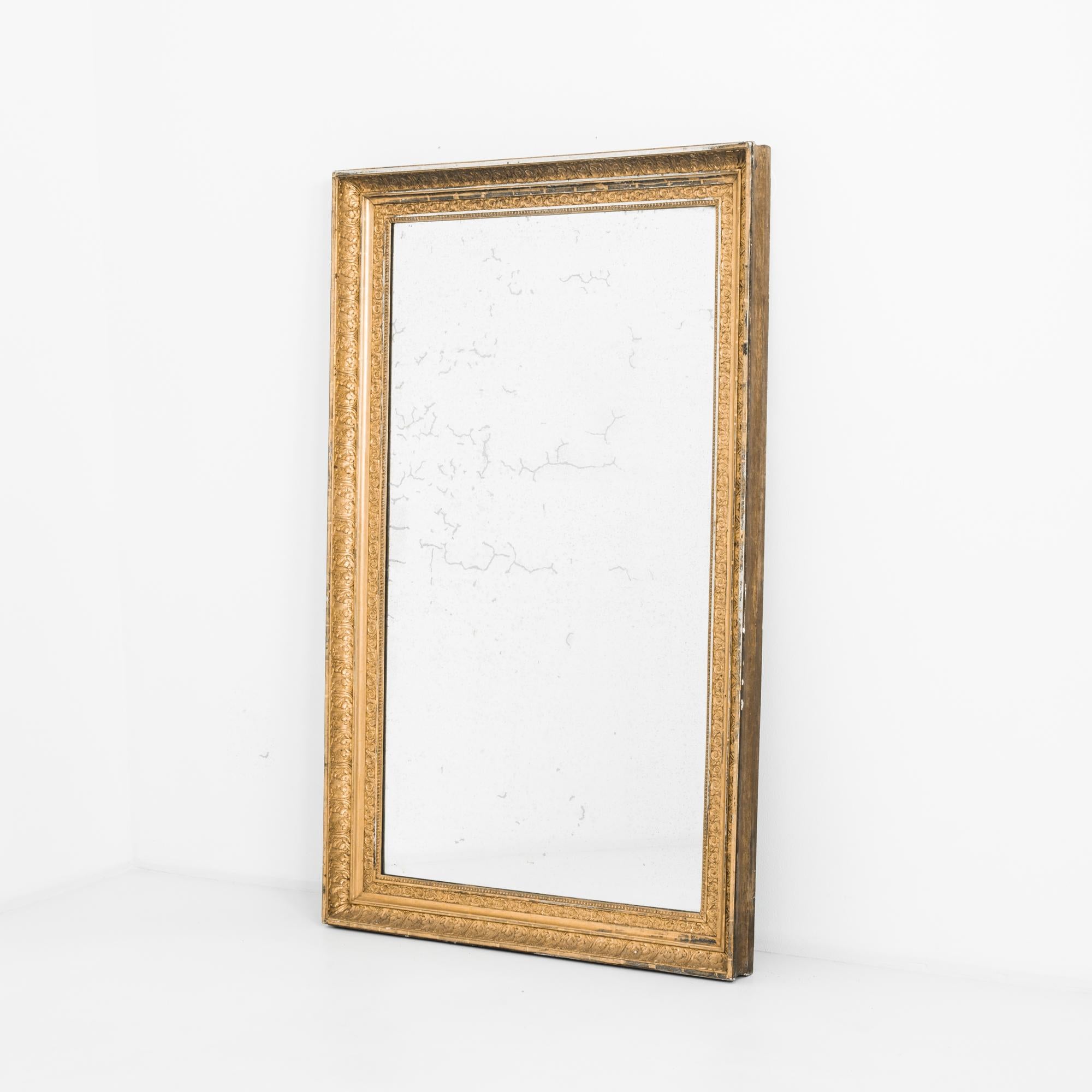 A wooden mirror produced in France circa 1880. This gilt, antique mirror, measuring five and a half feet tall, features an ornate leaf motif around its deep frame. As a looking glass produced in the height of the Aesthetic Movement, it is meant to