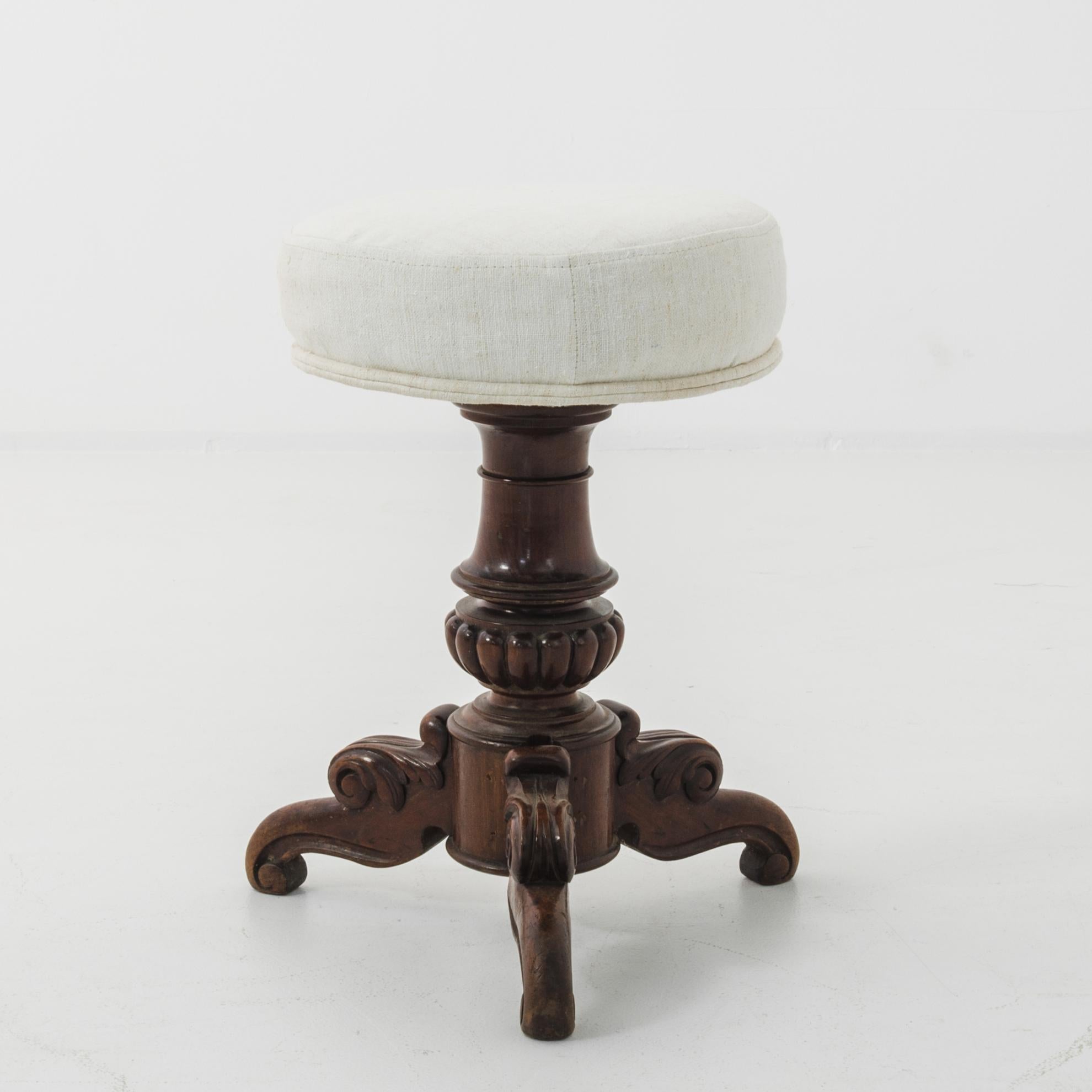 This wooden stool, adjusting with a metal screw, was made in France, circa 1880. Neoclassical elements are on display in the carved ornamentation of gadroons on the turned stand, as well as the scrolls and leaves on the tripod legs. An upholstered