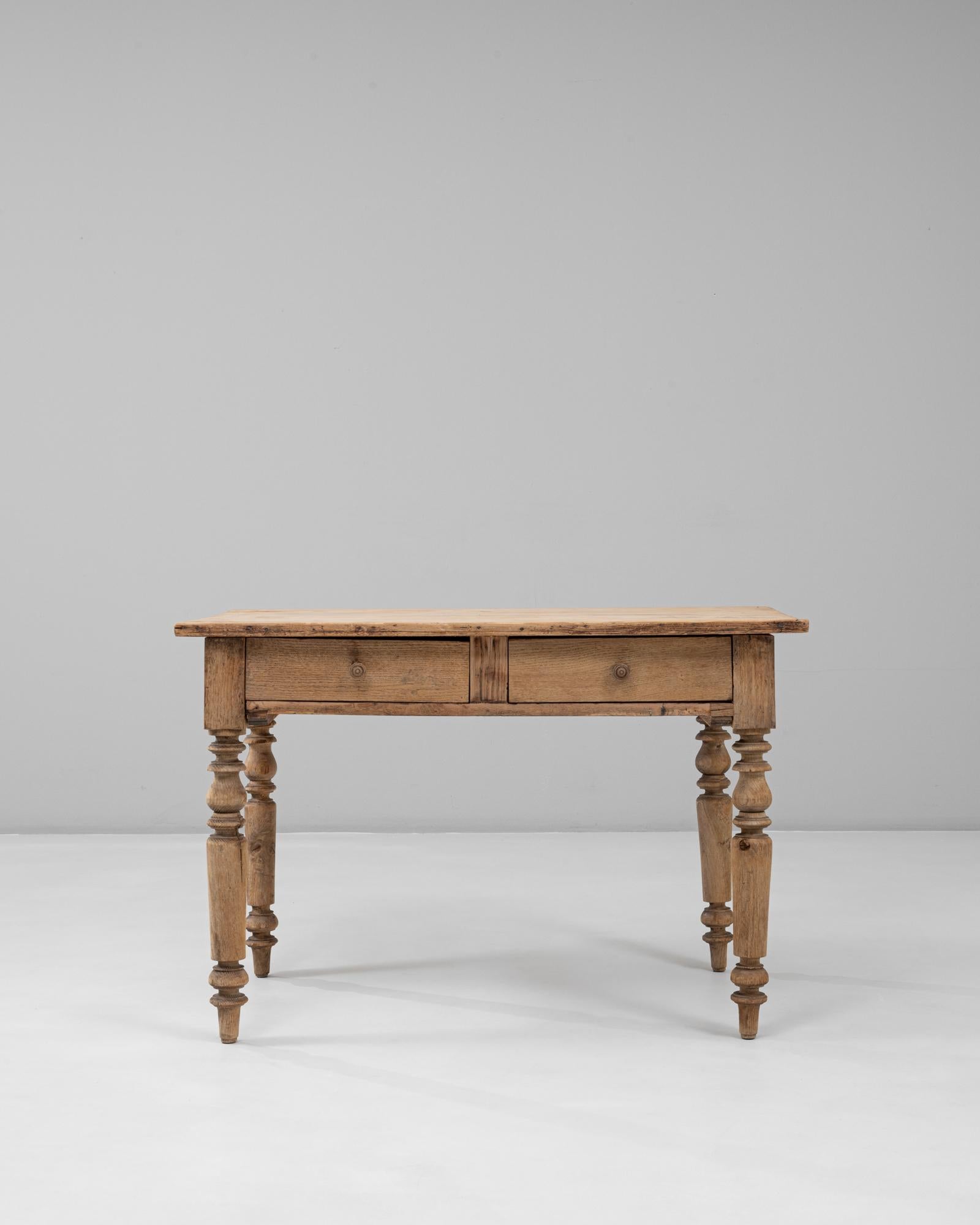 This 1880s French wooden writing table exudes rustic charm and timeless craftsmanship. Constructed from solid wood with a naturally aged patina, it features a rectangular top and two functional drawers that offer convenient storage. The turned legs,