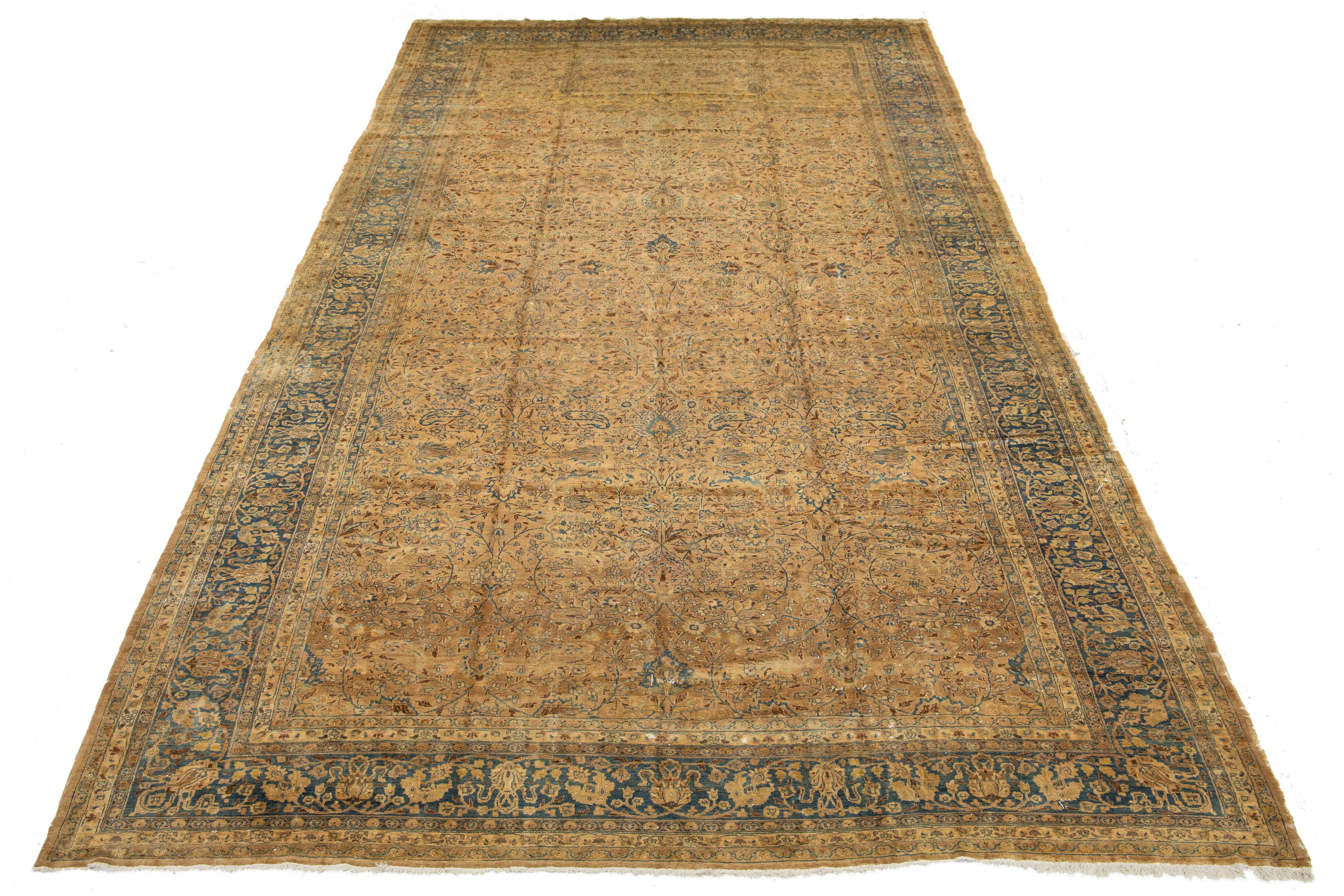 Dieser schöne übergroße antike Mashad-Teppich aus handgeknüpfter Wolle hat eine hellbraune Feldfarbe. Der Perserteppich hat einen blauen Rahmen und blaue Akzente und zeigt ein wunderschönes klassisches Blumenmuster.

Dieser Teppich misst 10'7