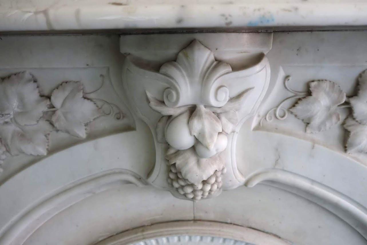 Intricately hand carved white Carrara marble mantel with grape and vine details and slight gray veining from the 1880s. It is pictured here in its original New York City home. This mantel comes with a complete cast iron summer cover. The mantel