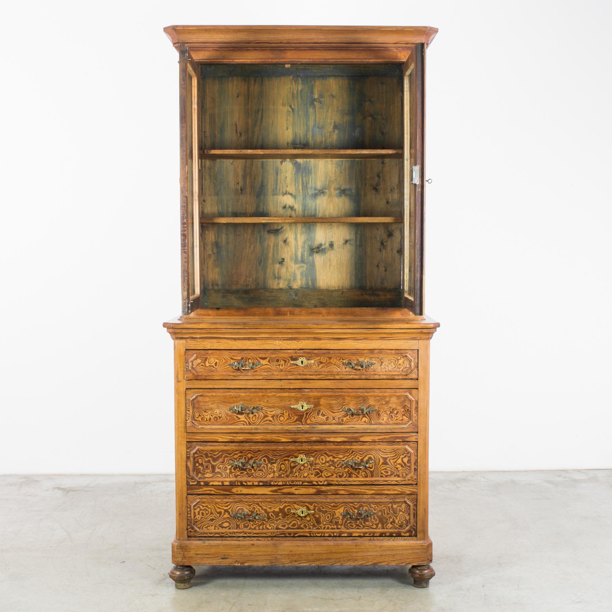 A beautiful pine vitrine, made in France, circa 1880. It houses a display cabinet with three shelves above a chest of four drawers. The interior of the display cabinet is stained blue, highlighting the deep golden hue of the wood. Raised on onion