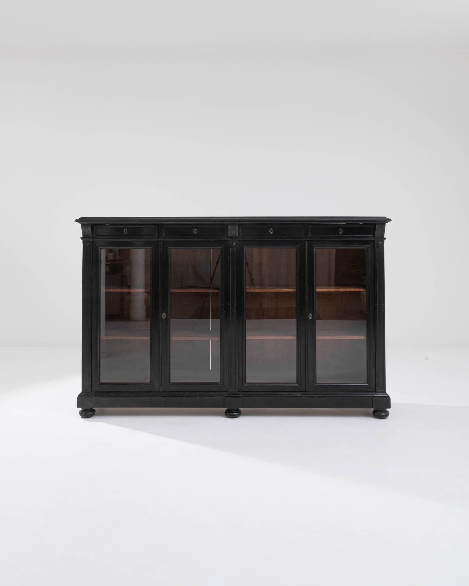 A wooden vitrine made in France, circa 1880. Two sets of glass-paned doors swing outwards, granting access to four spacious and adjustable shelves, above which sit four drawers. The dark finish, typical of the Napoleon III style, has ebbed away here