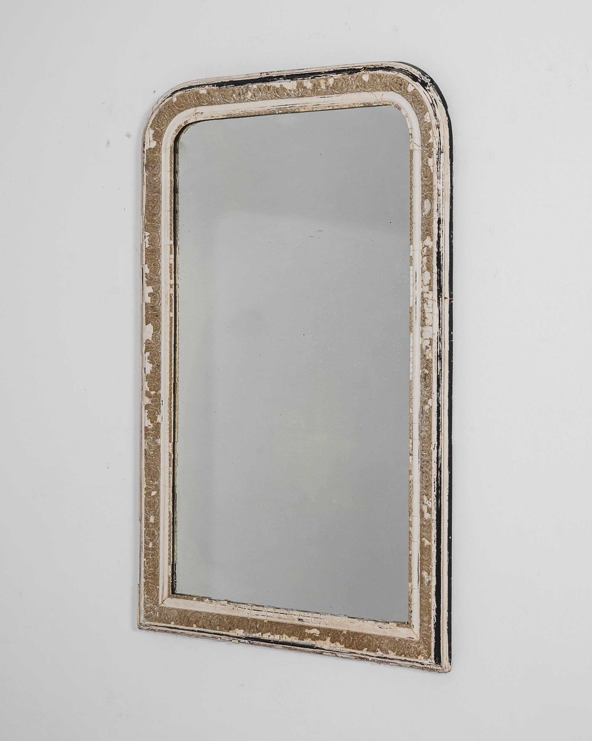 A wood and plaster frame mirror from France, produced circa 1880. A wall mounted antique mirror standing three and a half feet tall, featuring rounded corner corners at the top and floral motif reliefs around the frame. Age lines, silver spots and