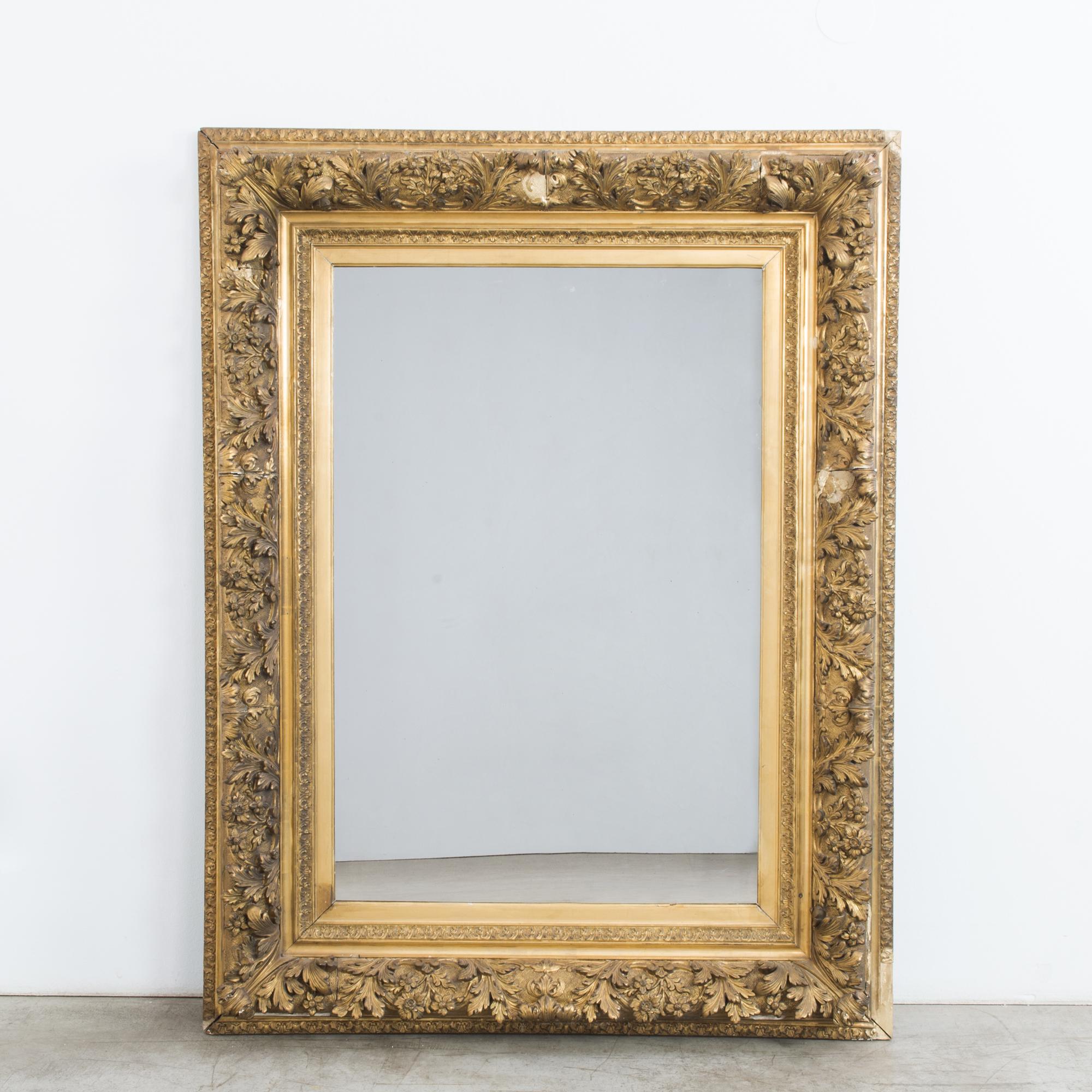 A gilded mirror from France, circa 1880. Luxuriant rococo carving dances across the wide borders of the frame, full of vitality and detail. Unfurling leaves and dainty flowers give an impression of natural variation and exuberance, elevated by the